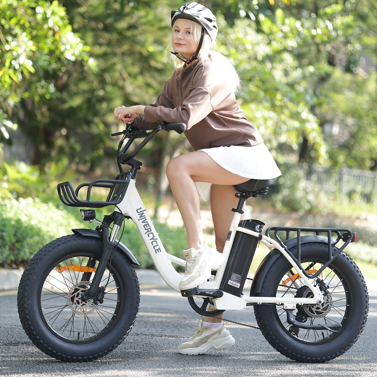 Kobieta w kasku siedzi na białym rowerze elektrycznym z grubymi oponami na zewnątrz.