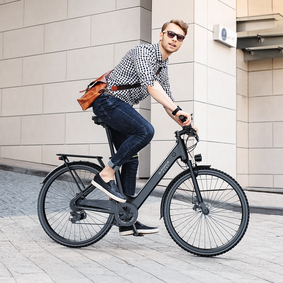 Mężczyzna na czarnym rowerze jedzie po wybrukowanej ulicy przed budynkiem.