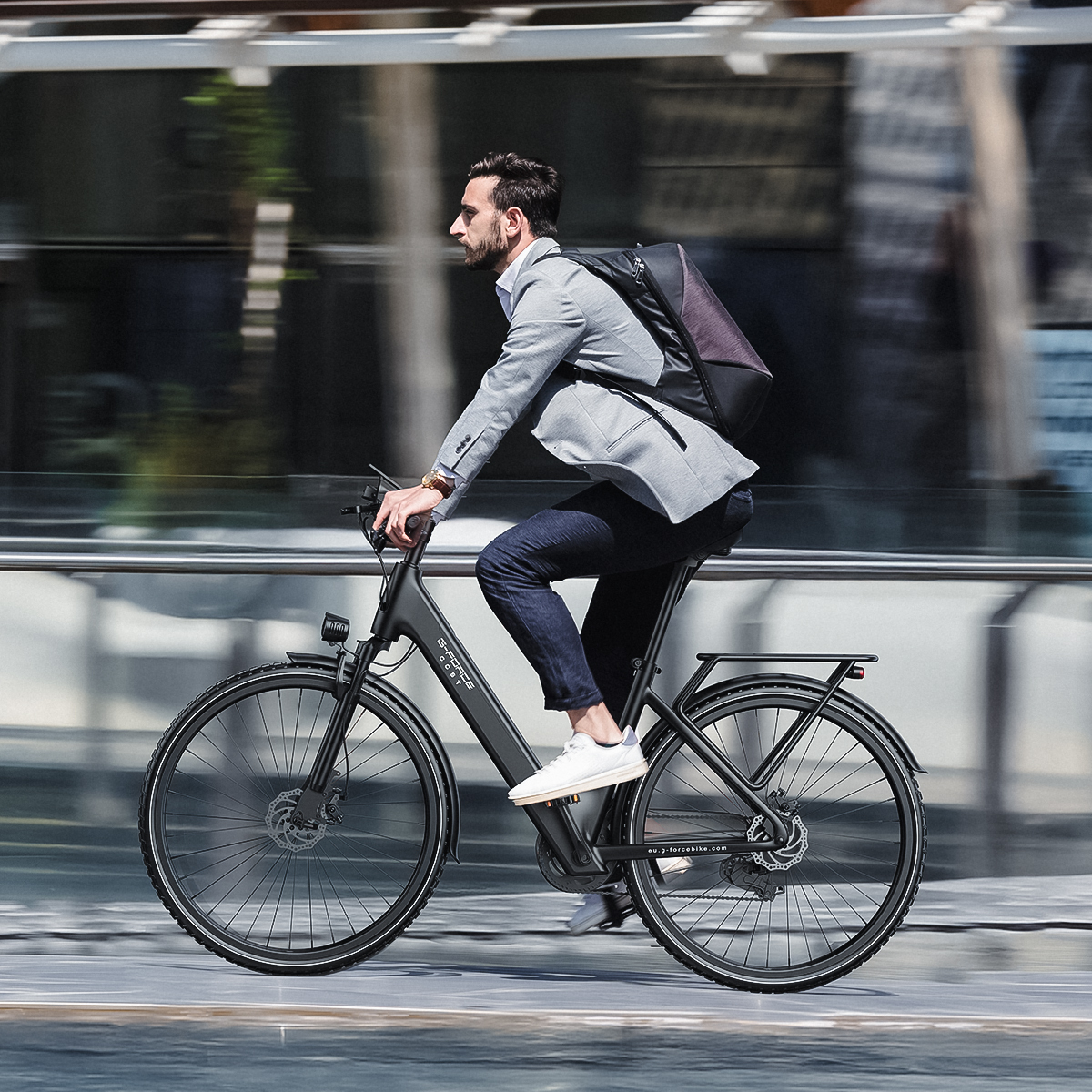 Mężczyzna w szarym garniturze jedzie na czarnym rowerze z plecakiem.