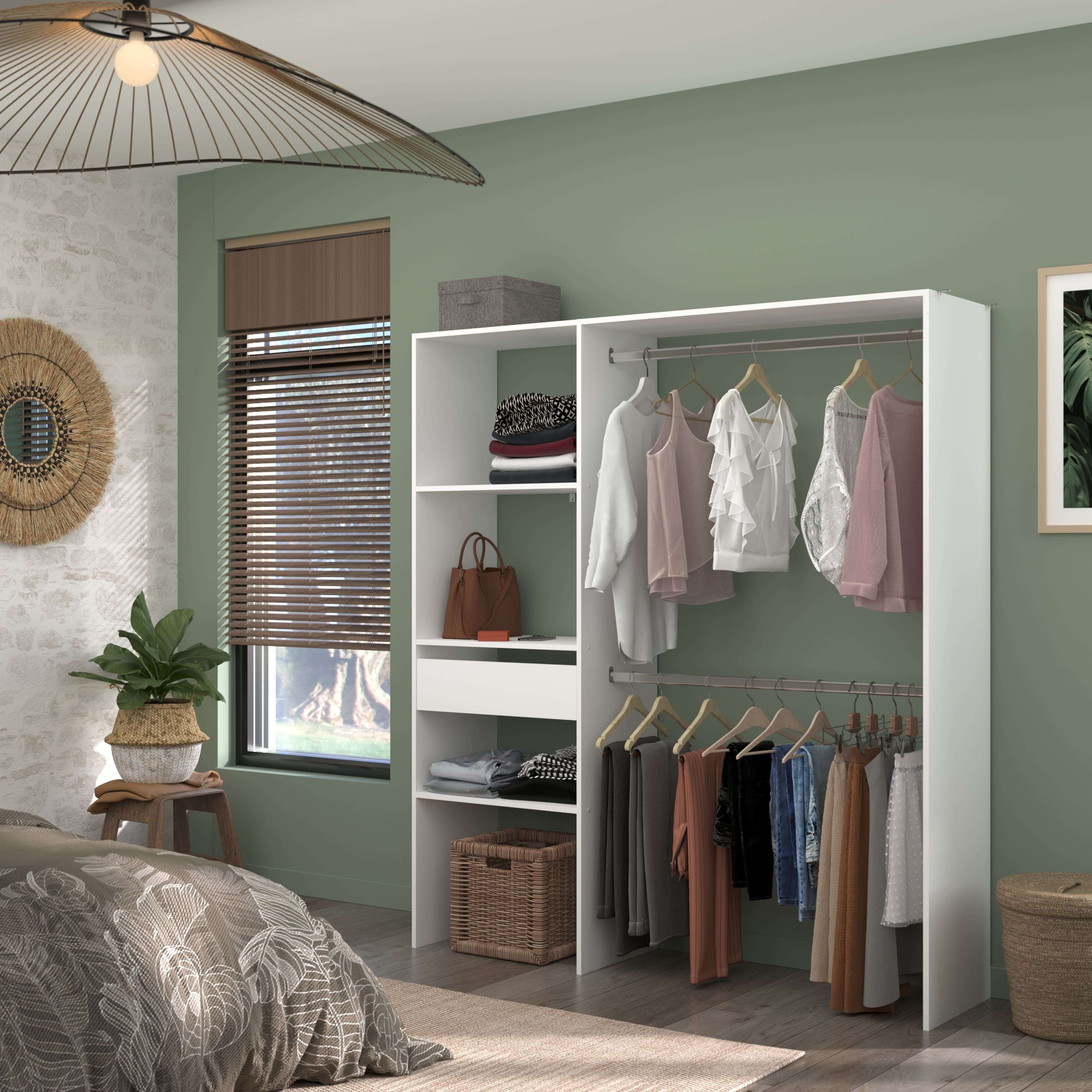 Un dormitorio con paredes verde claro y un armario blanco abierto lleno de ropa. A la izquierda, una cama con un edredón estampado.