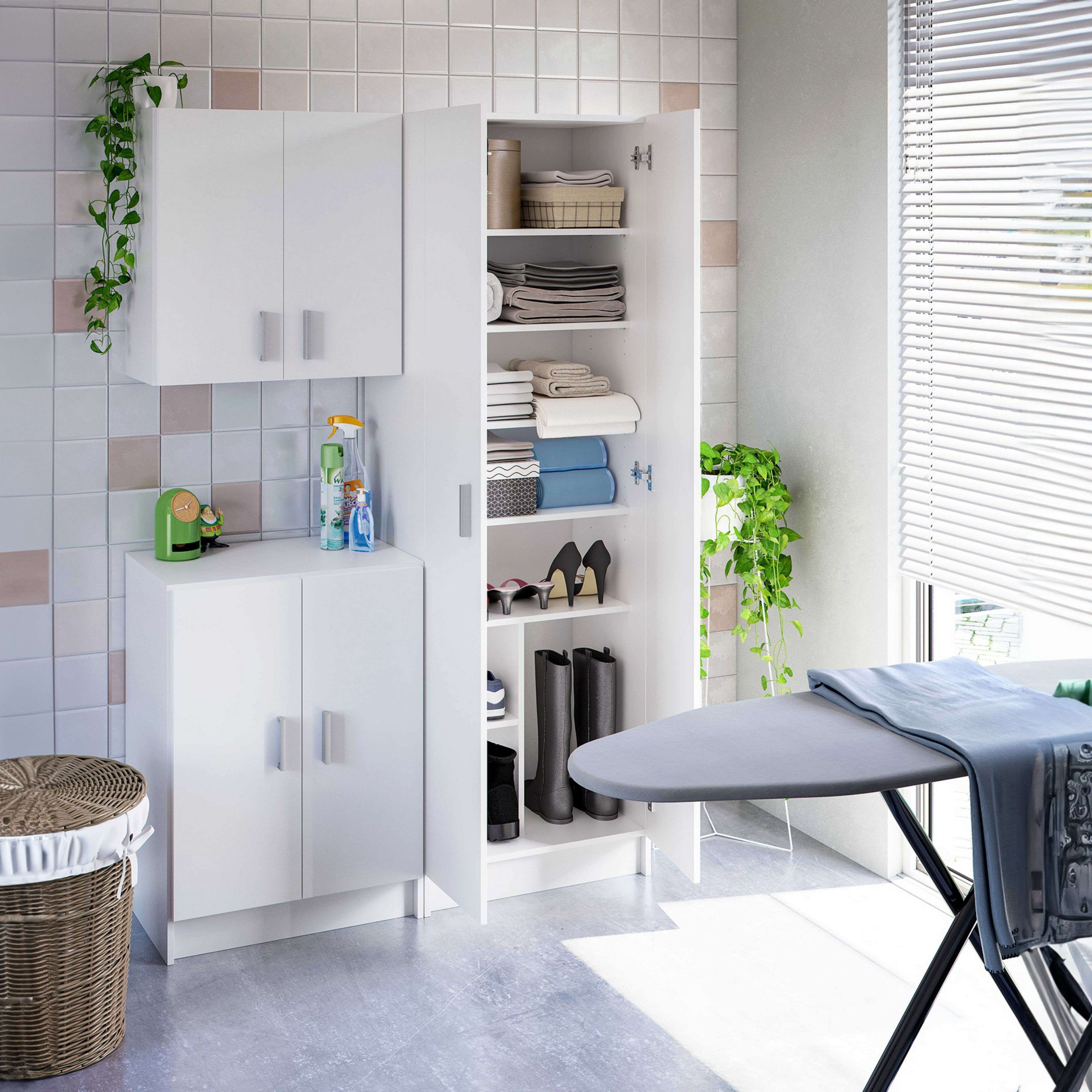 Un cuarto de lavandería con gabinetes blancos, cesta de mimbre, tabla de planchar y plantas.