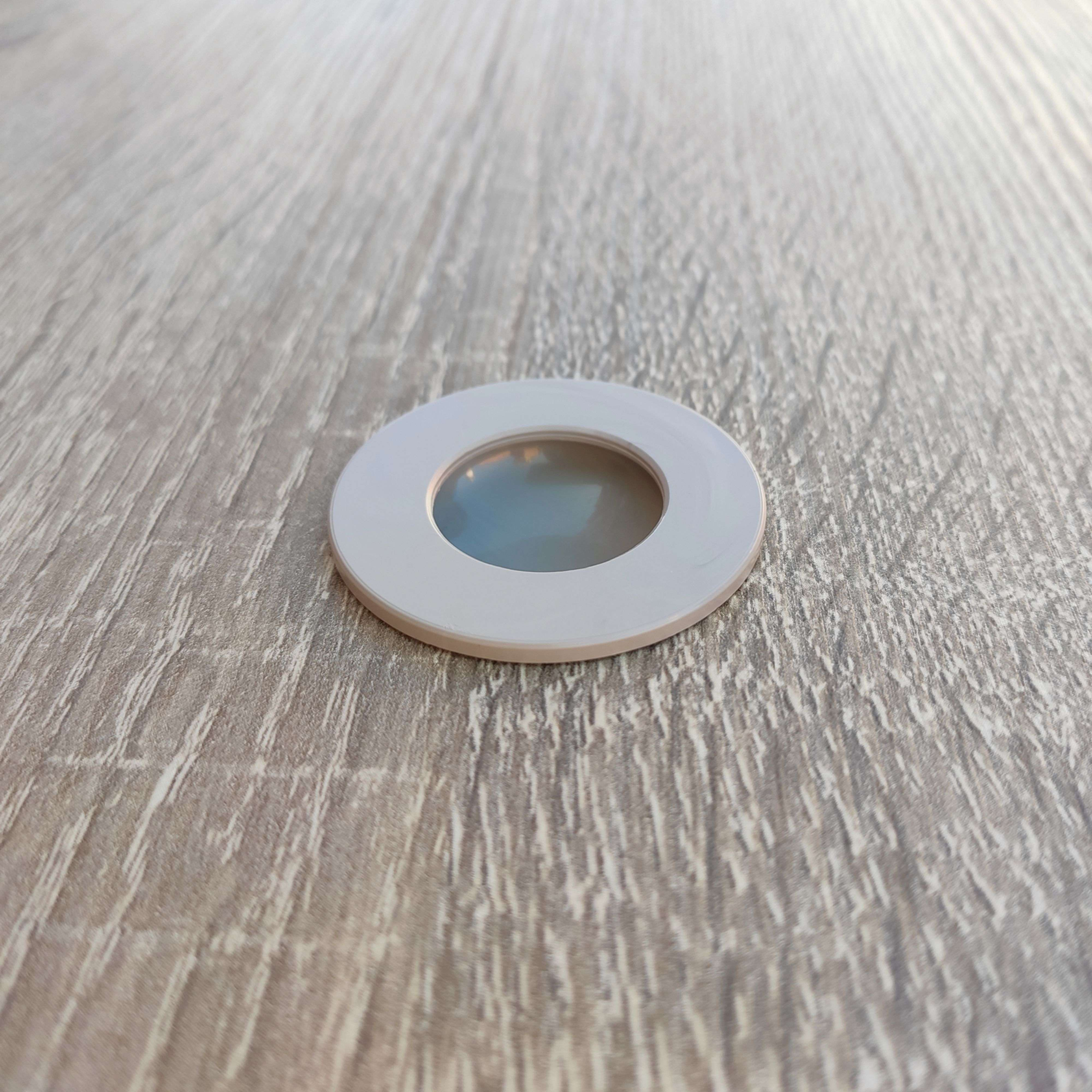 Un anillo blanco con una ventana circular de lente sobre una superficie de madera.
