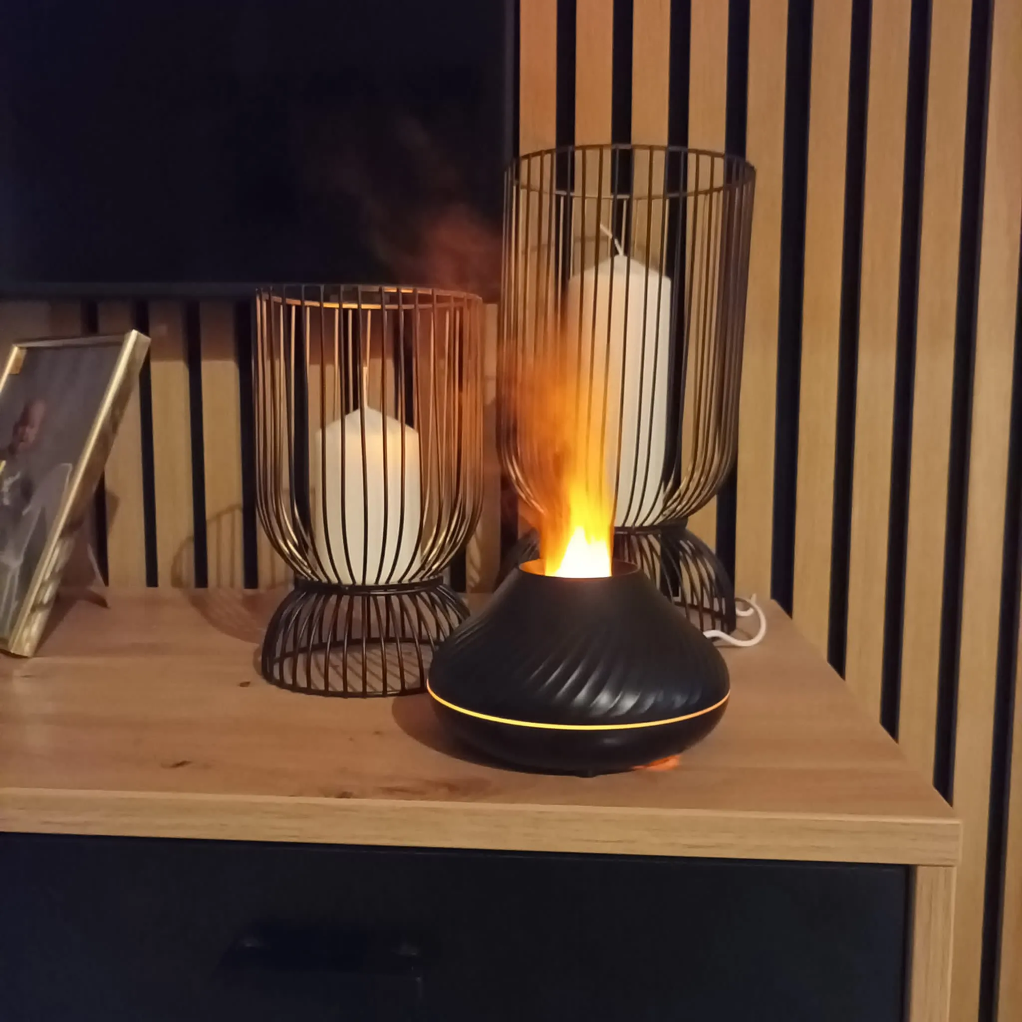 Ein schwarzer Diffusor mit Flammenmuster neben zwei Kerzenhaltern mit Kerzen.