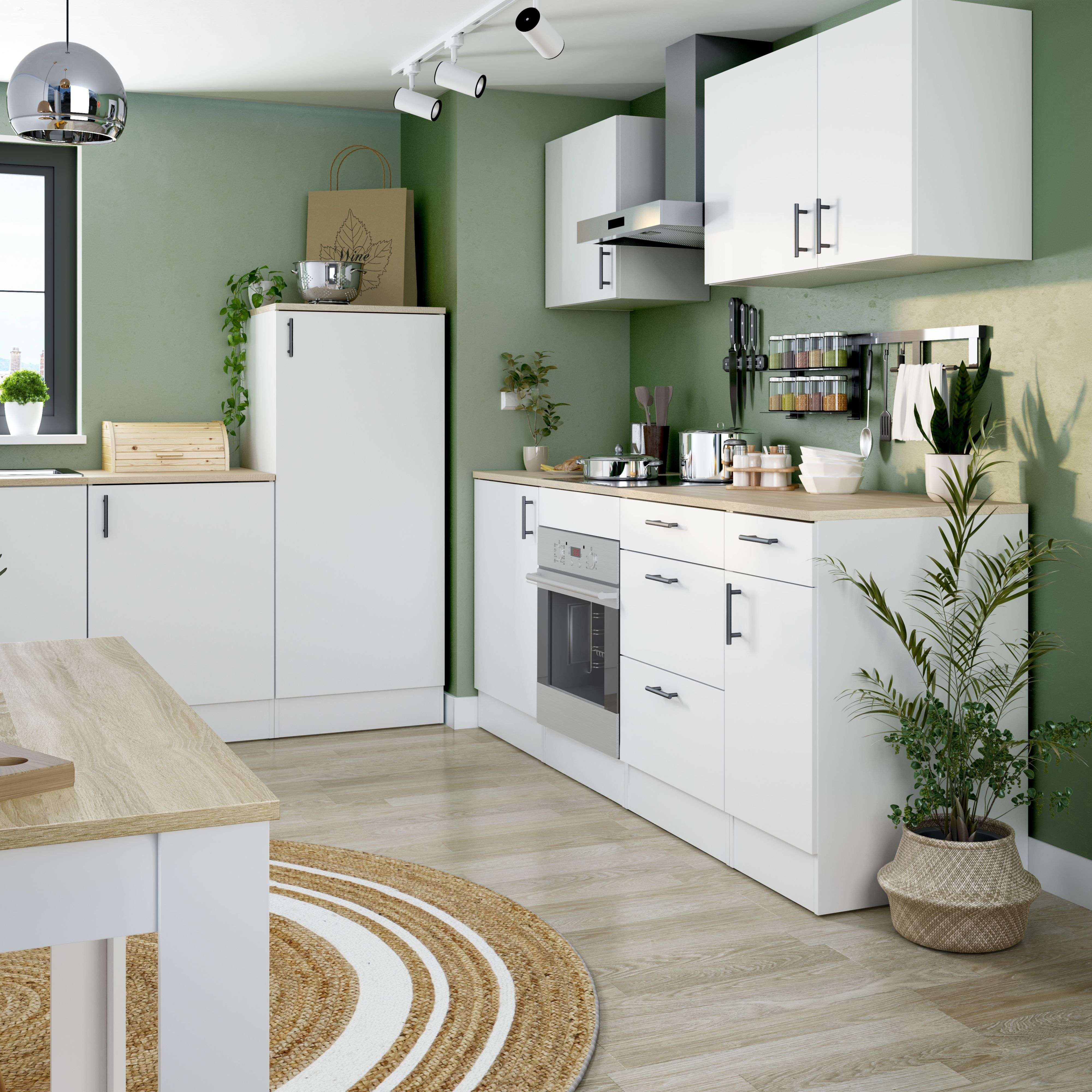 Moderna cocina verde con gabinetes blancos, pisos de madera y alfombra redonda.