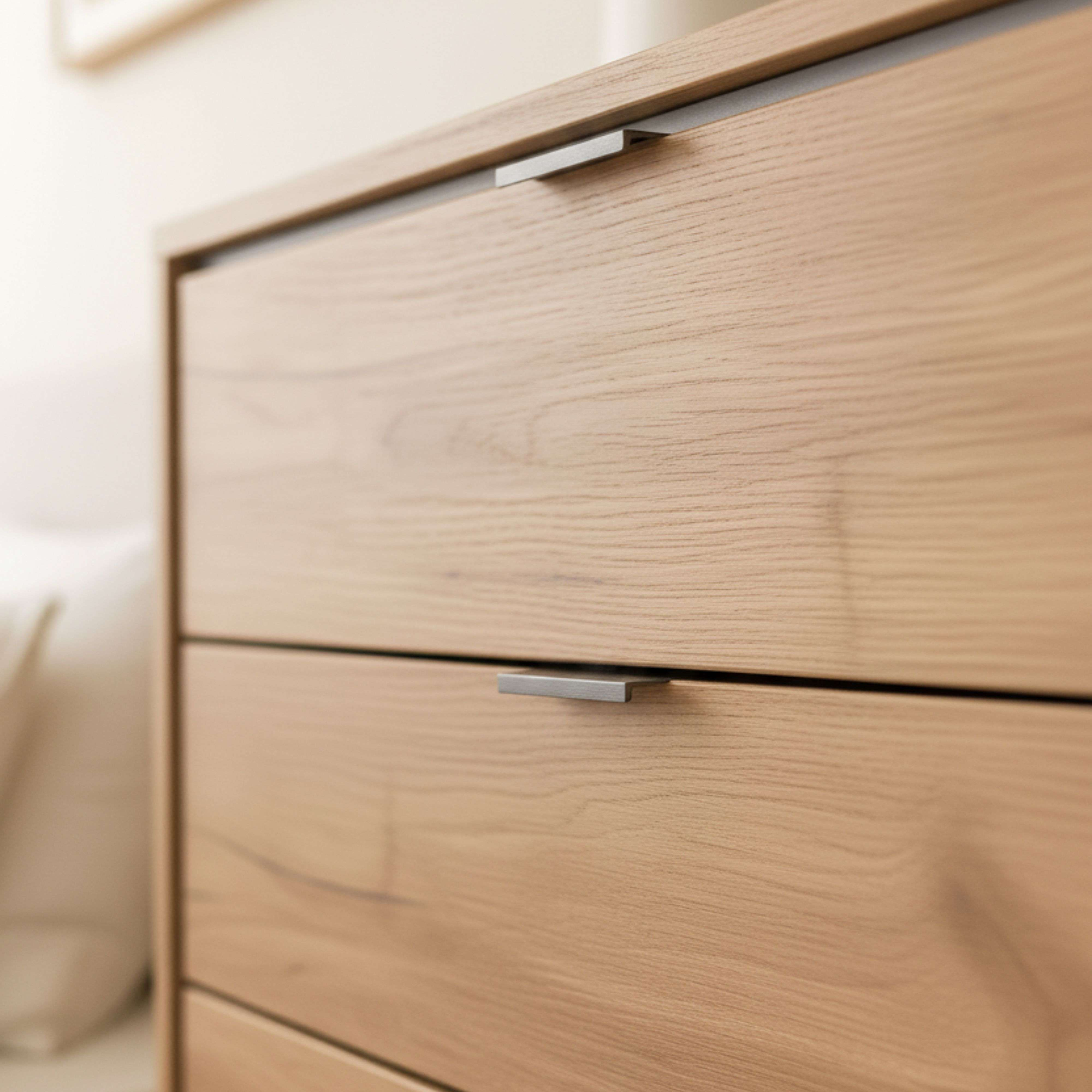 Primer plano de una cómoda de madera con tres cajones y tiradores plateados.