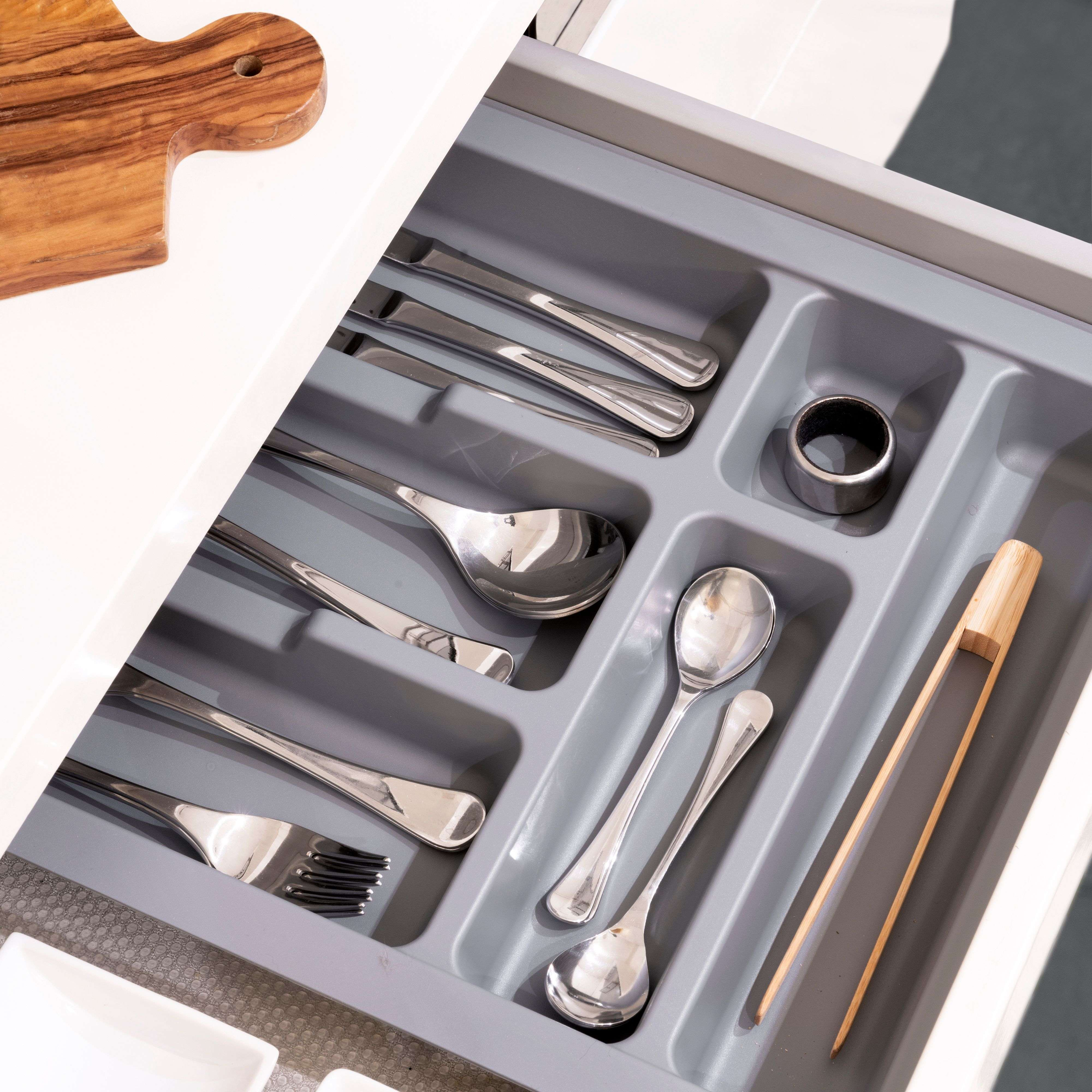 Cajón de cubiertos con cucharas, tenedores, cuchillos plateados y pinzas de madera.