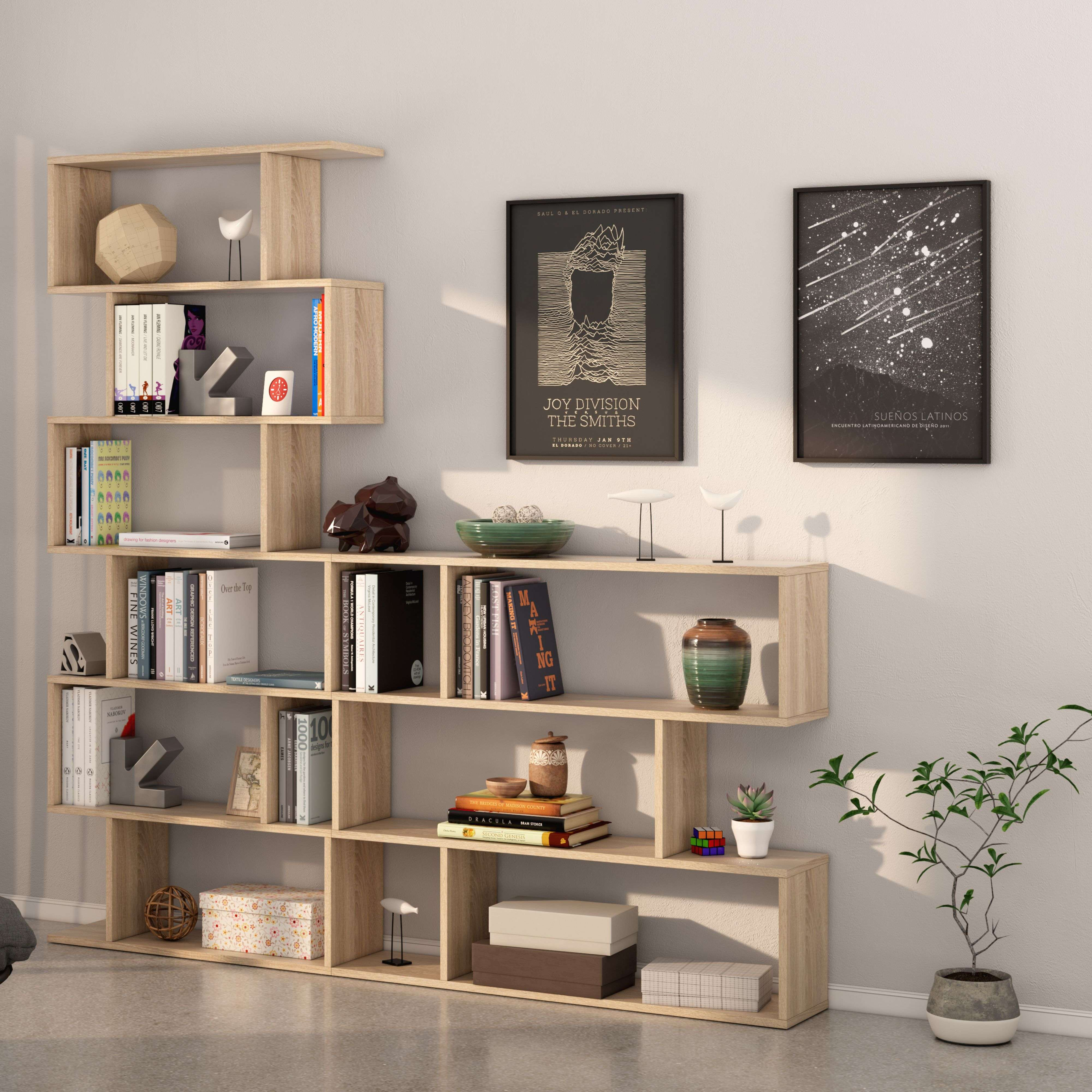 Estantería de madera clara con libros, arte y decoración. Dos pósters cuelgan en la pared.