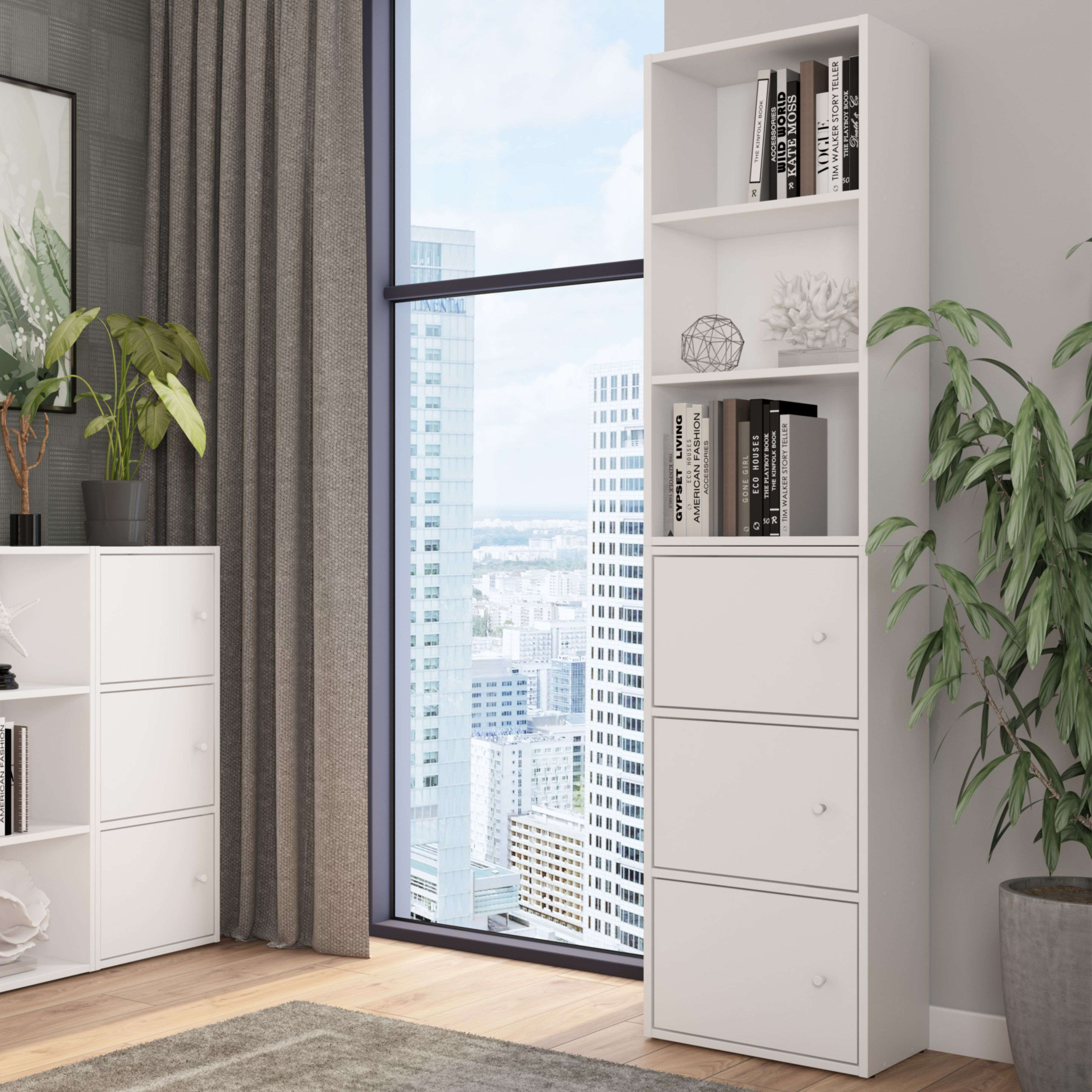 Una estantería blanca con libros y decoración, junto a una ventana con vistas a la ciudad.