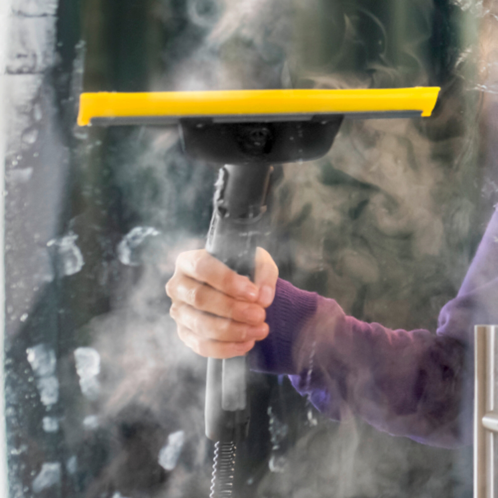 Una mano tiene un pulitore a vapore con un tergipavimento giallo, che spruzza vapore.