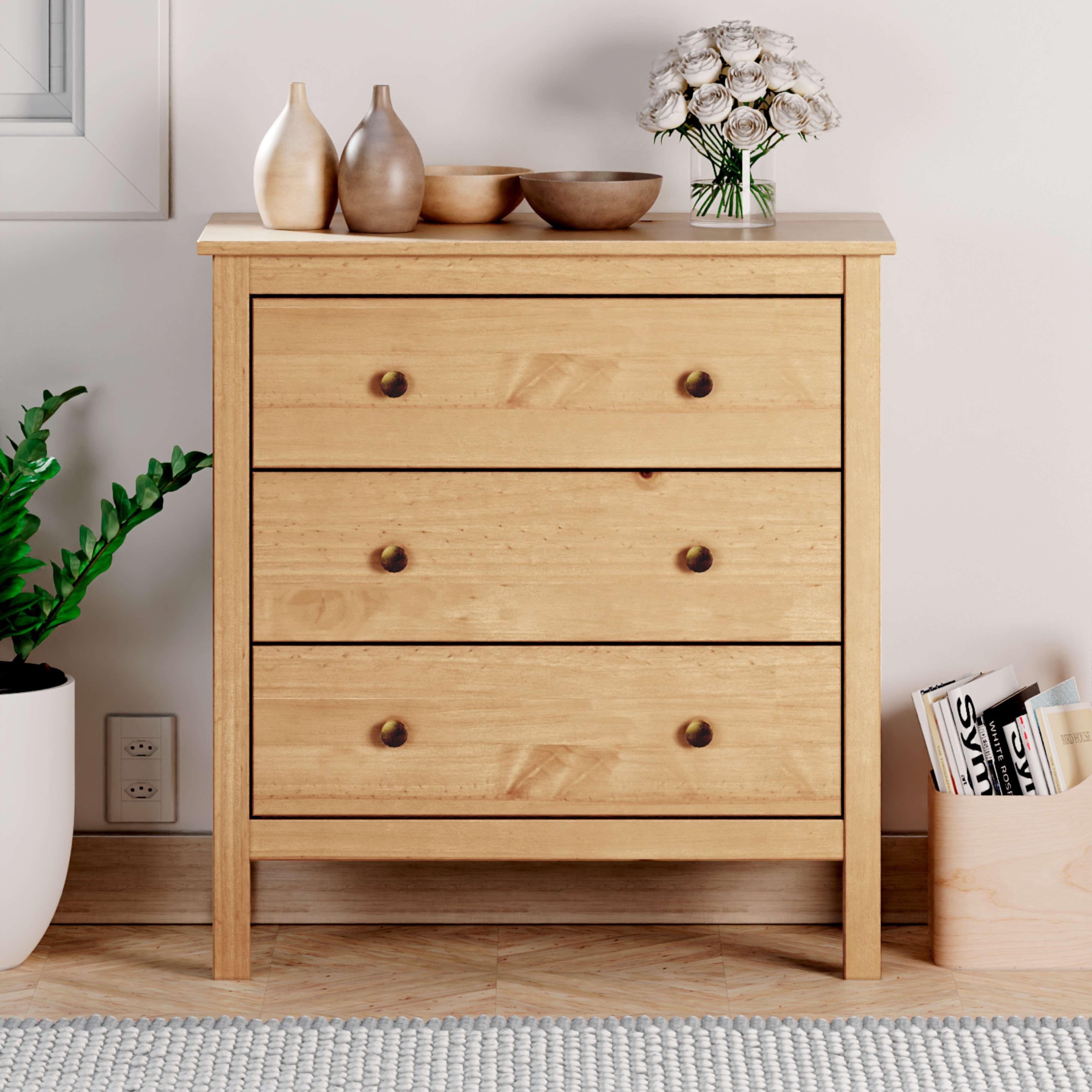 Cómoda de madera con tres cajones, decorada con jarrones y flores.