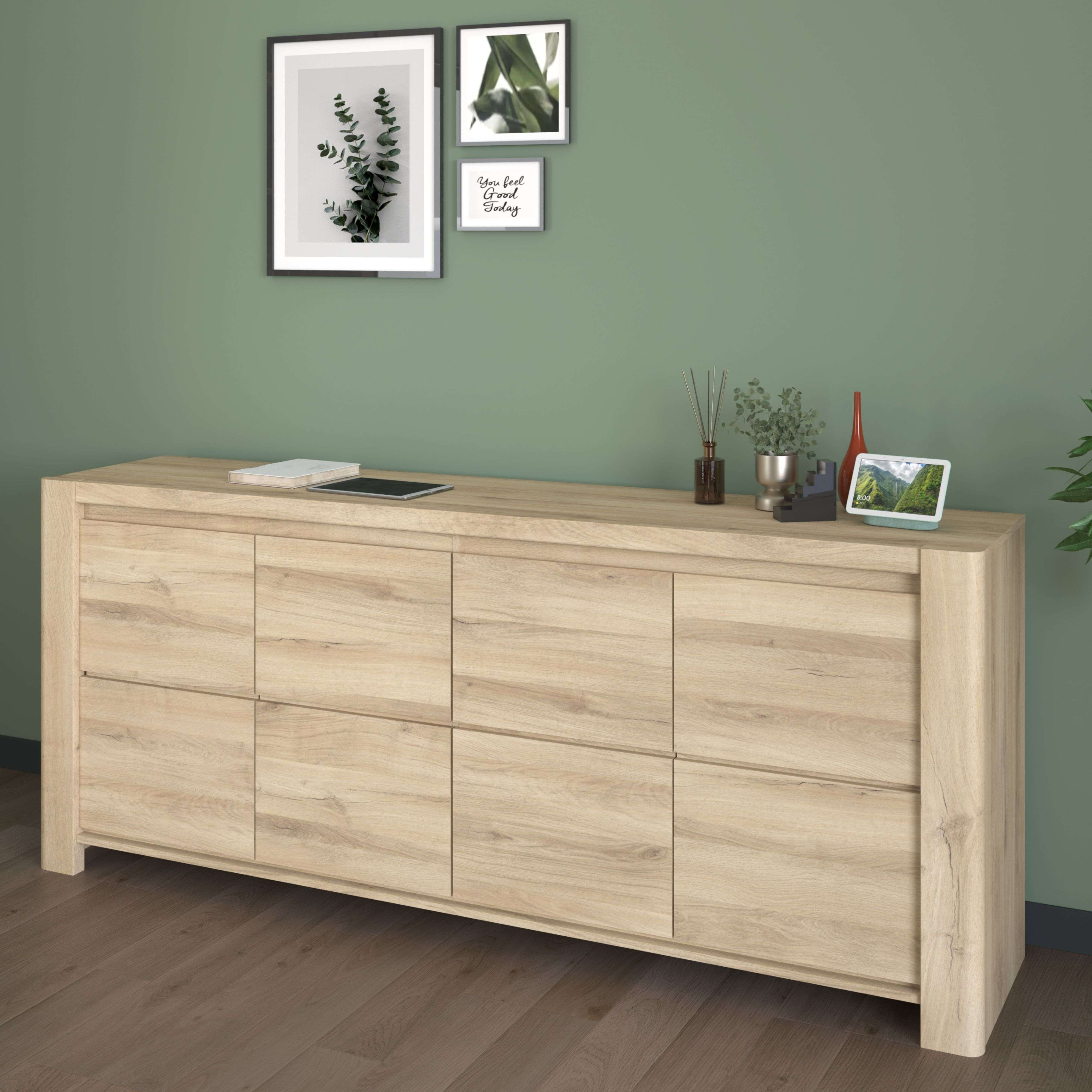 Un aparador de madera clara con decoración y cuadros en una pared verde.
