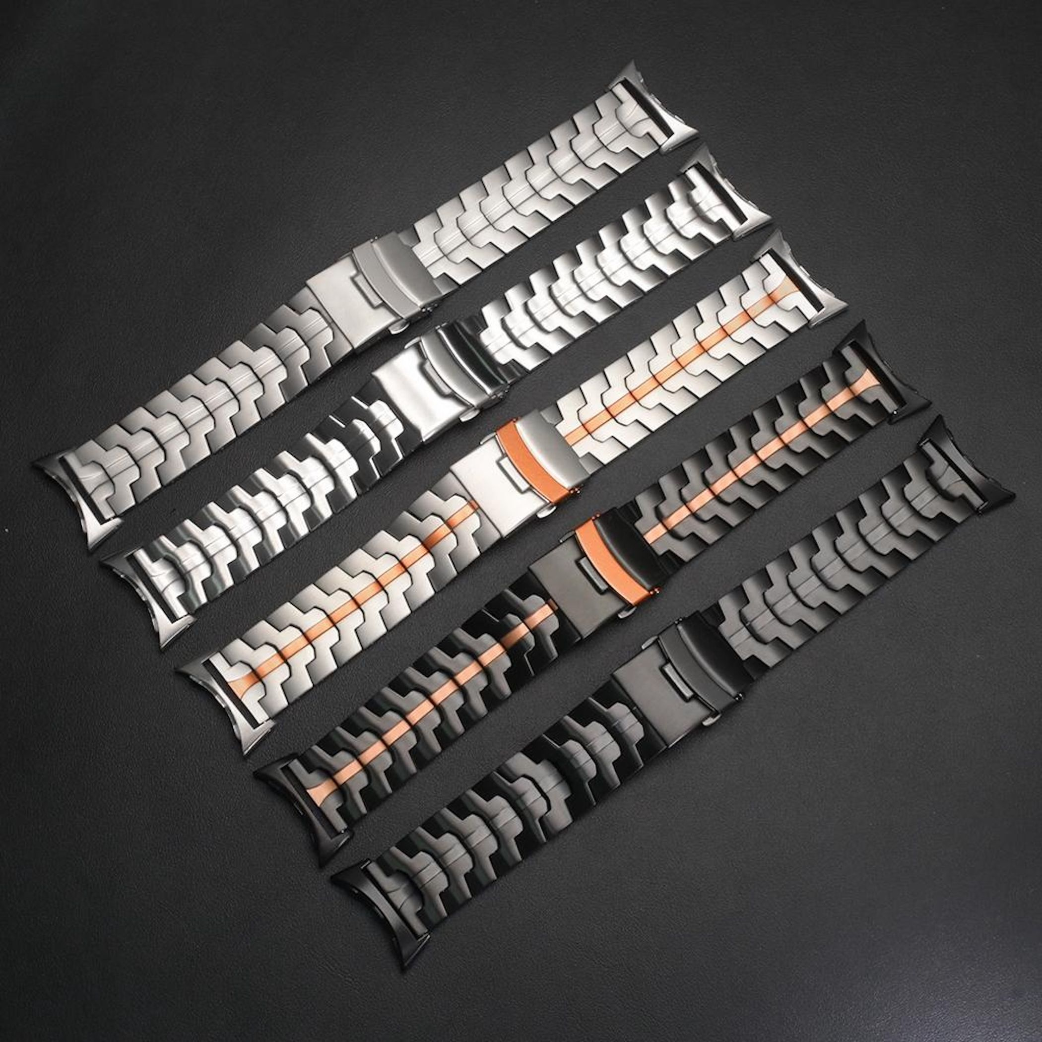 Fünf Edelstahl-Uhrenarmbänder mit orangen Akzenten liegen auf schwarzem Hintergrund.