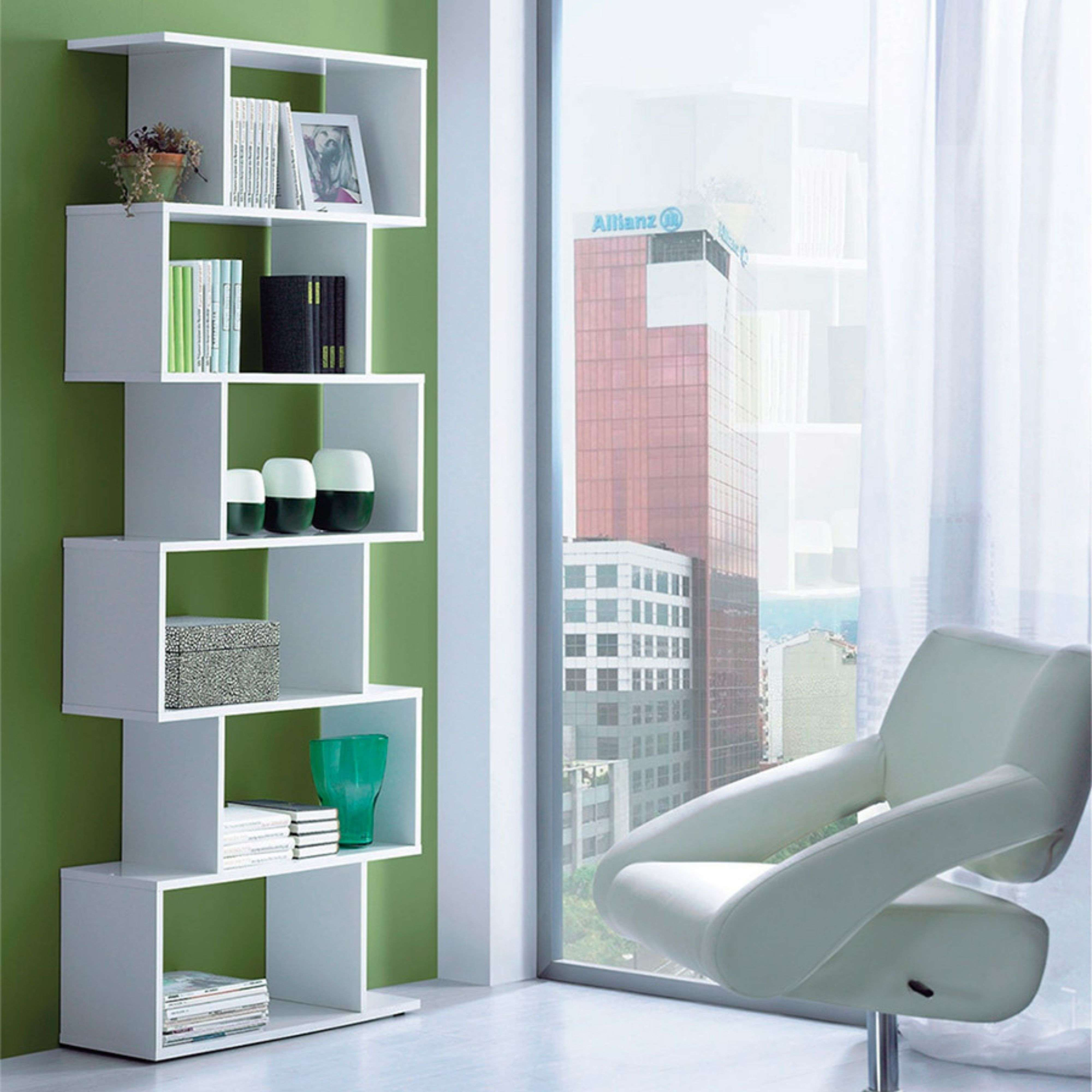 Una estantería blanca con libros, plantas y decoración frente a una ventana con vistas a la ciudad.