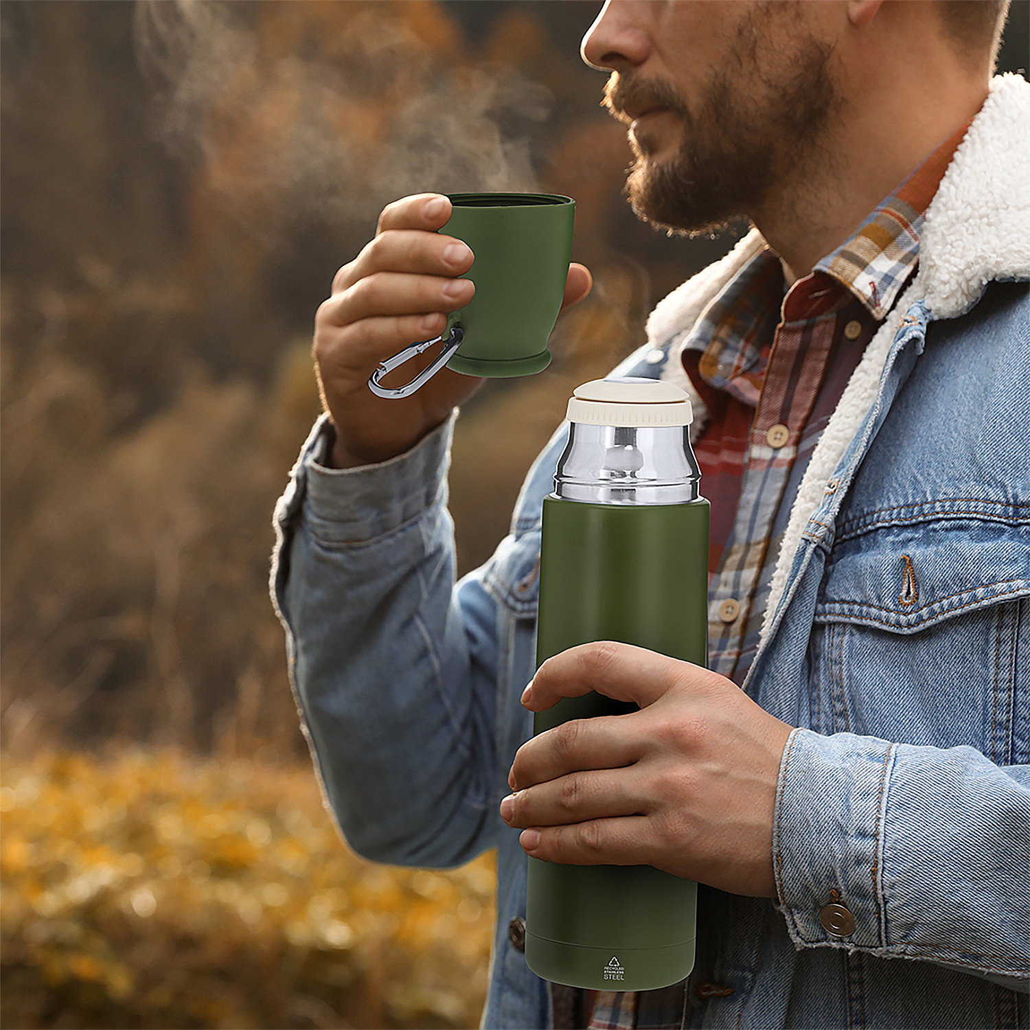 Mann trinkt aus grüner Tasse neben grünem Thermos. Rauch steigt auf.