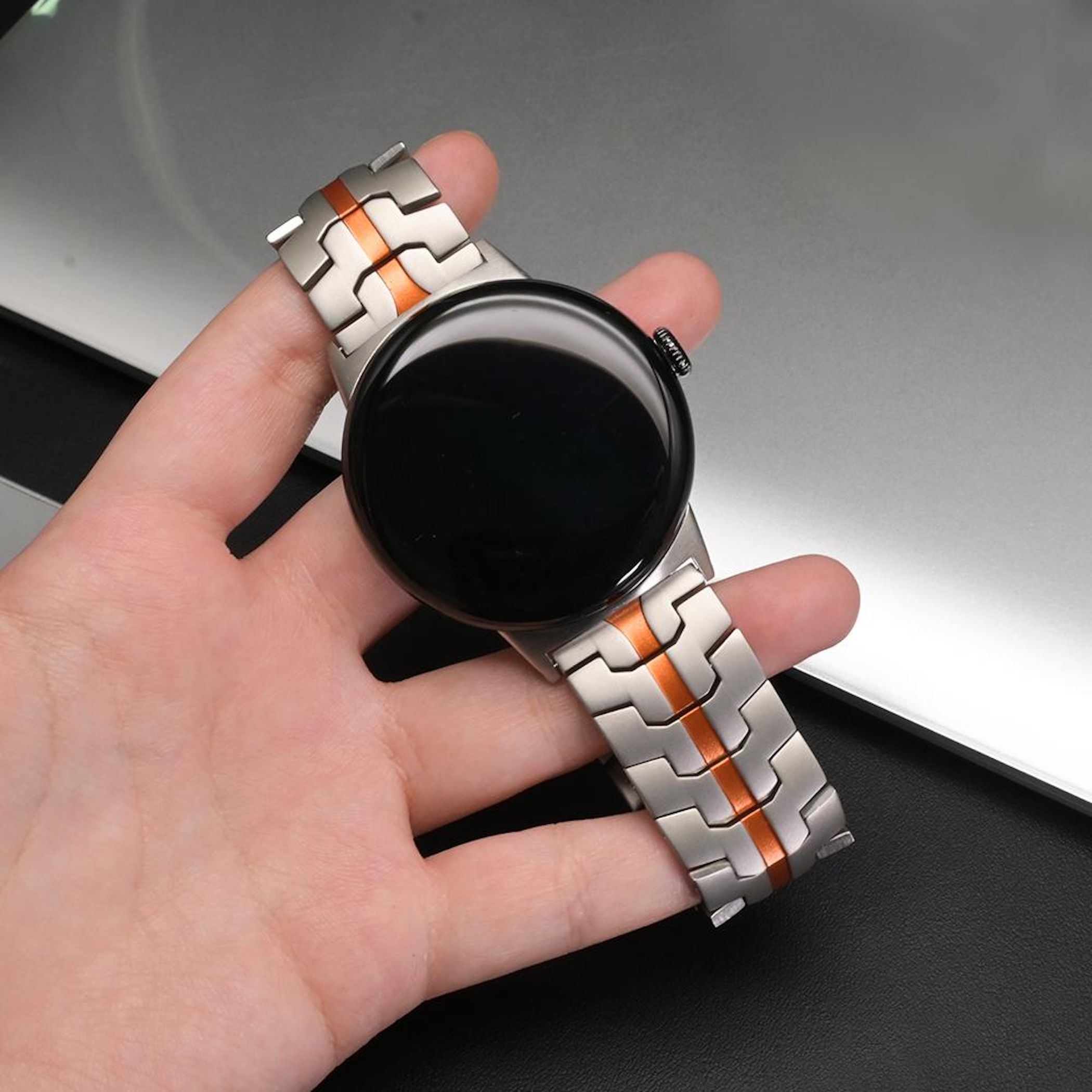 Eine Hand hält eine silberne und orangefarbene Smartwatch mit schwarzem Zifferblatt.