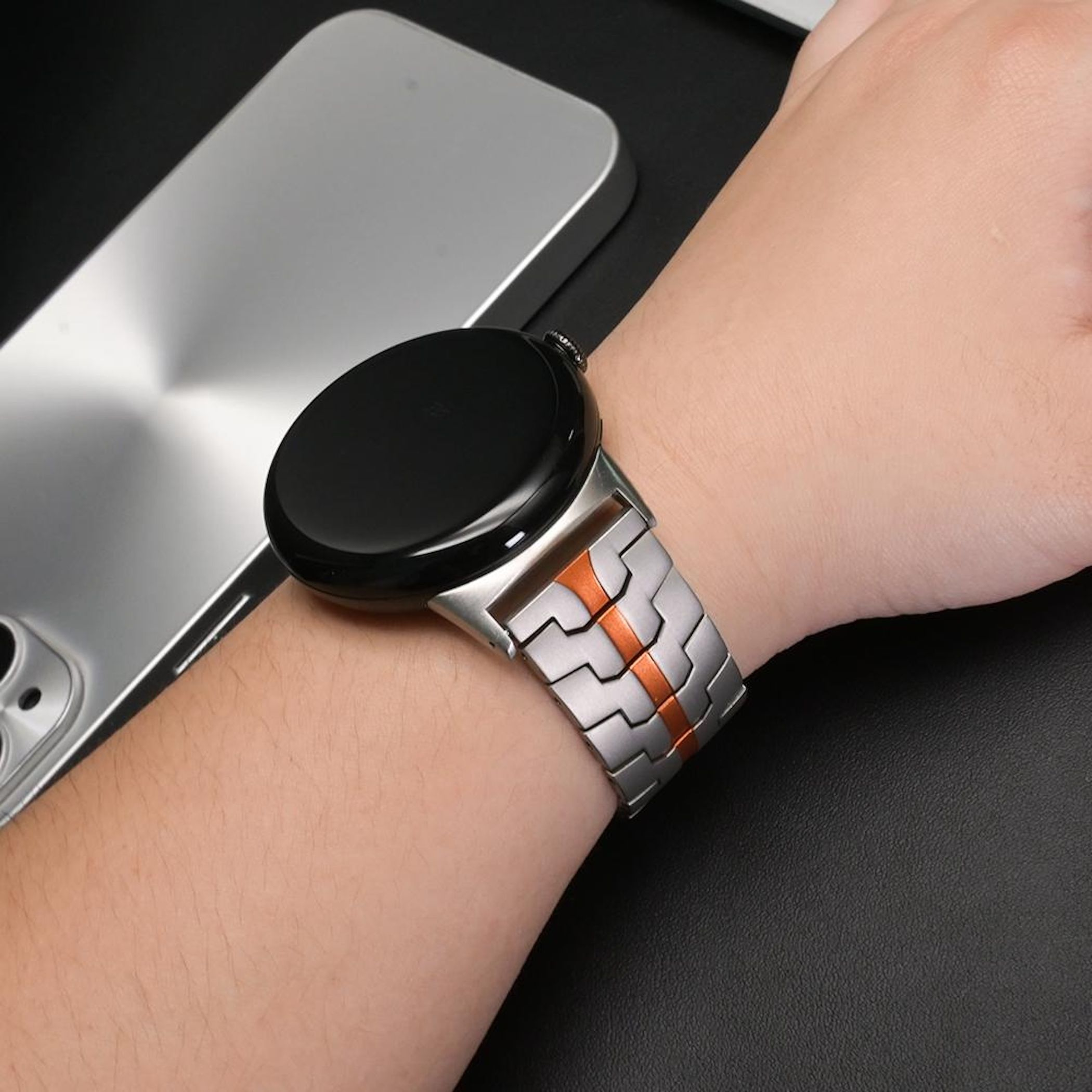 Arm mit Smartwatch und silbernem Armband mit orangefarbenen Akzenten.