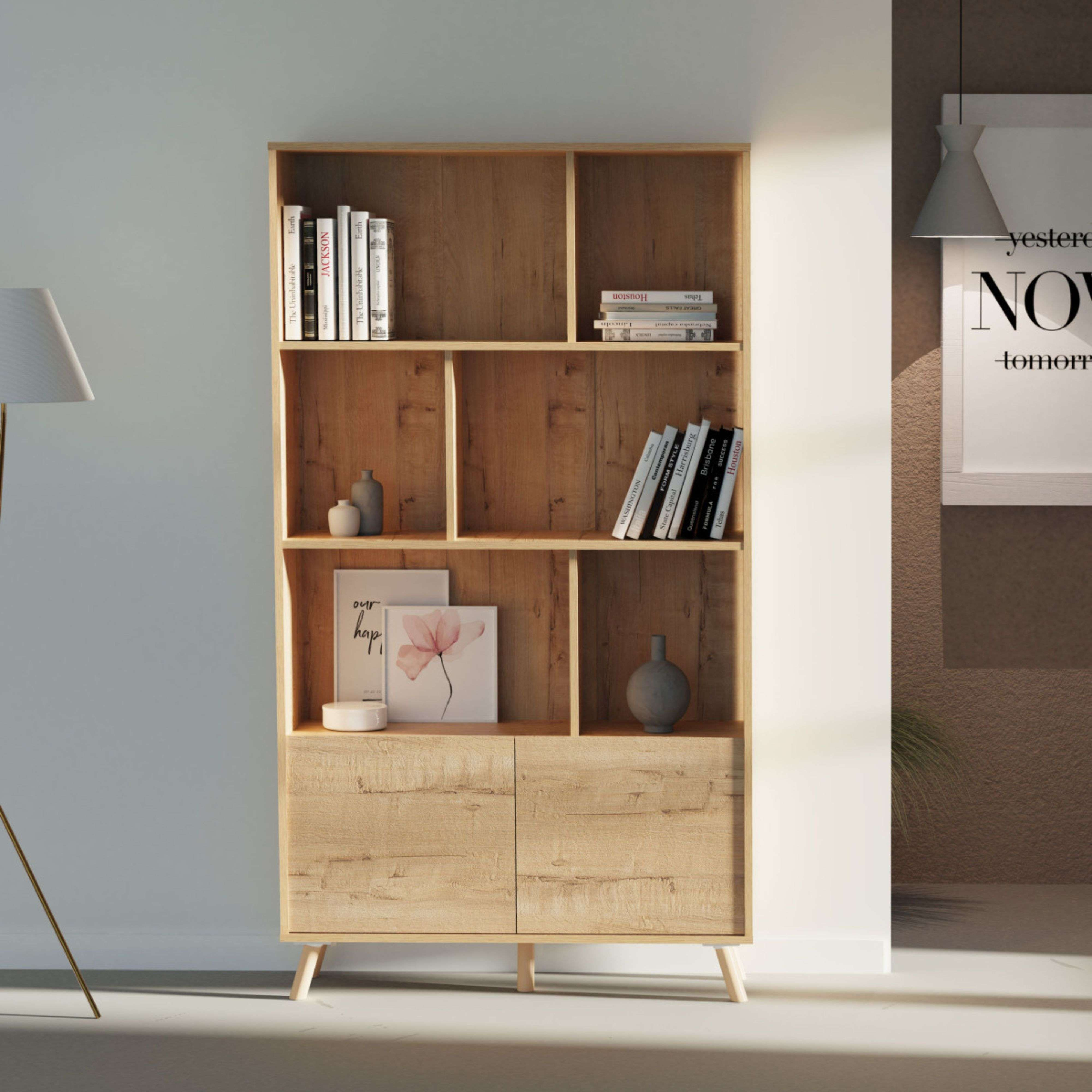 Una estantería de madera clara con libros y decoración, base de lámpara de pie y póster.