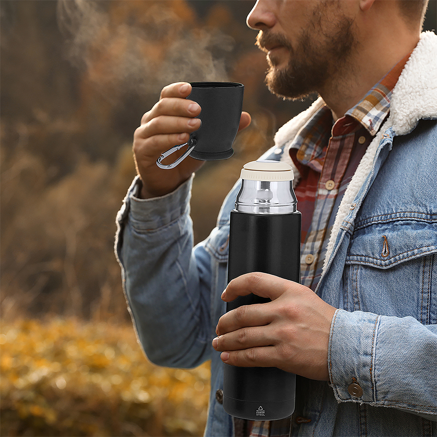 Mann trinkt aus schwarzer Tasse vor Thermoskanne, Herbstwald.
