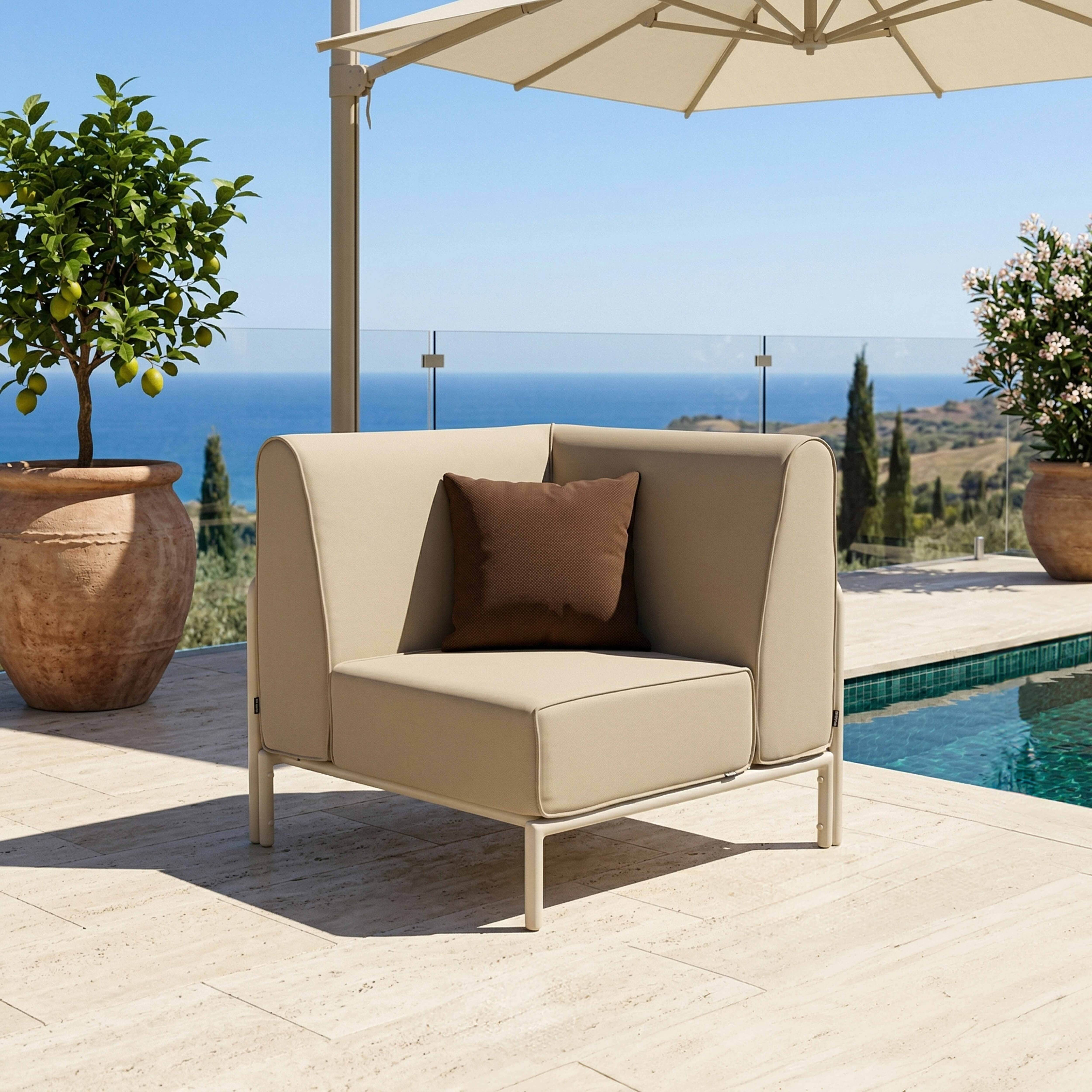 Ein beiger Sessel mit braunem Kissen steht auf einer Terrasse am Meer.
