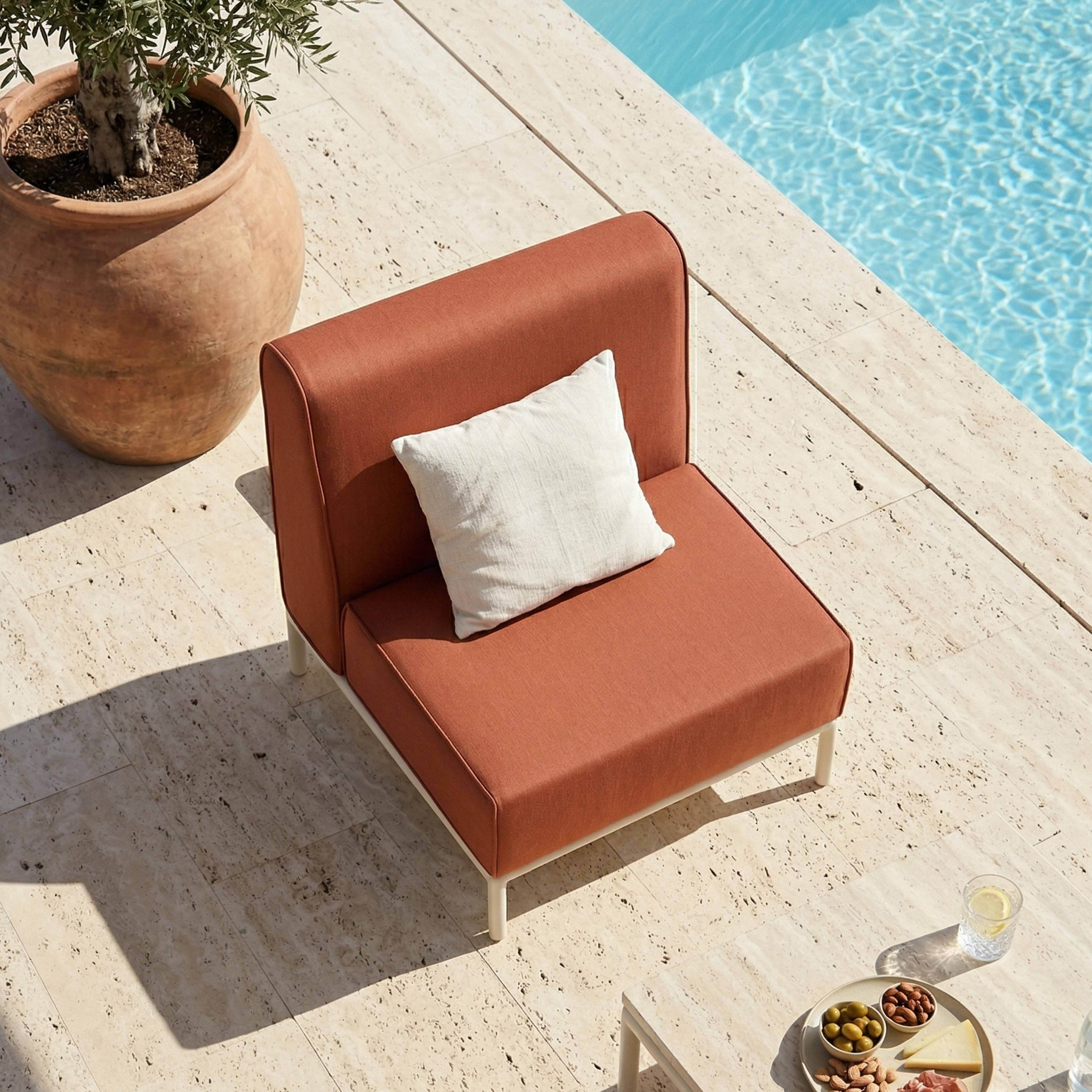Ein orangefarbener Sessel mit Kissen neben einem Pool, daneben ein Olivenbaum.