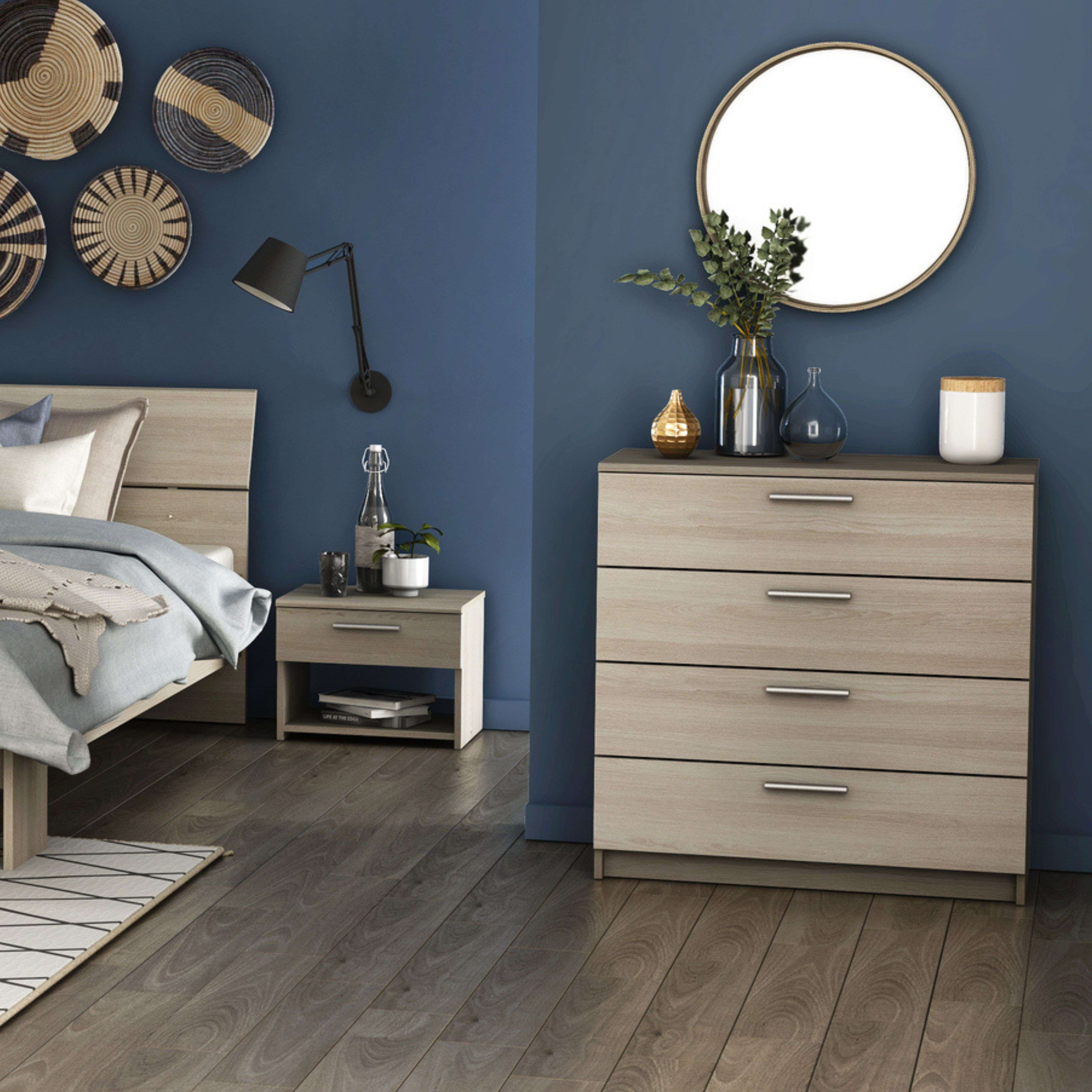 Un dormitorio con paredes azules, suelo de madera, cama, mesita y cómoda.