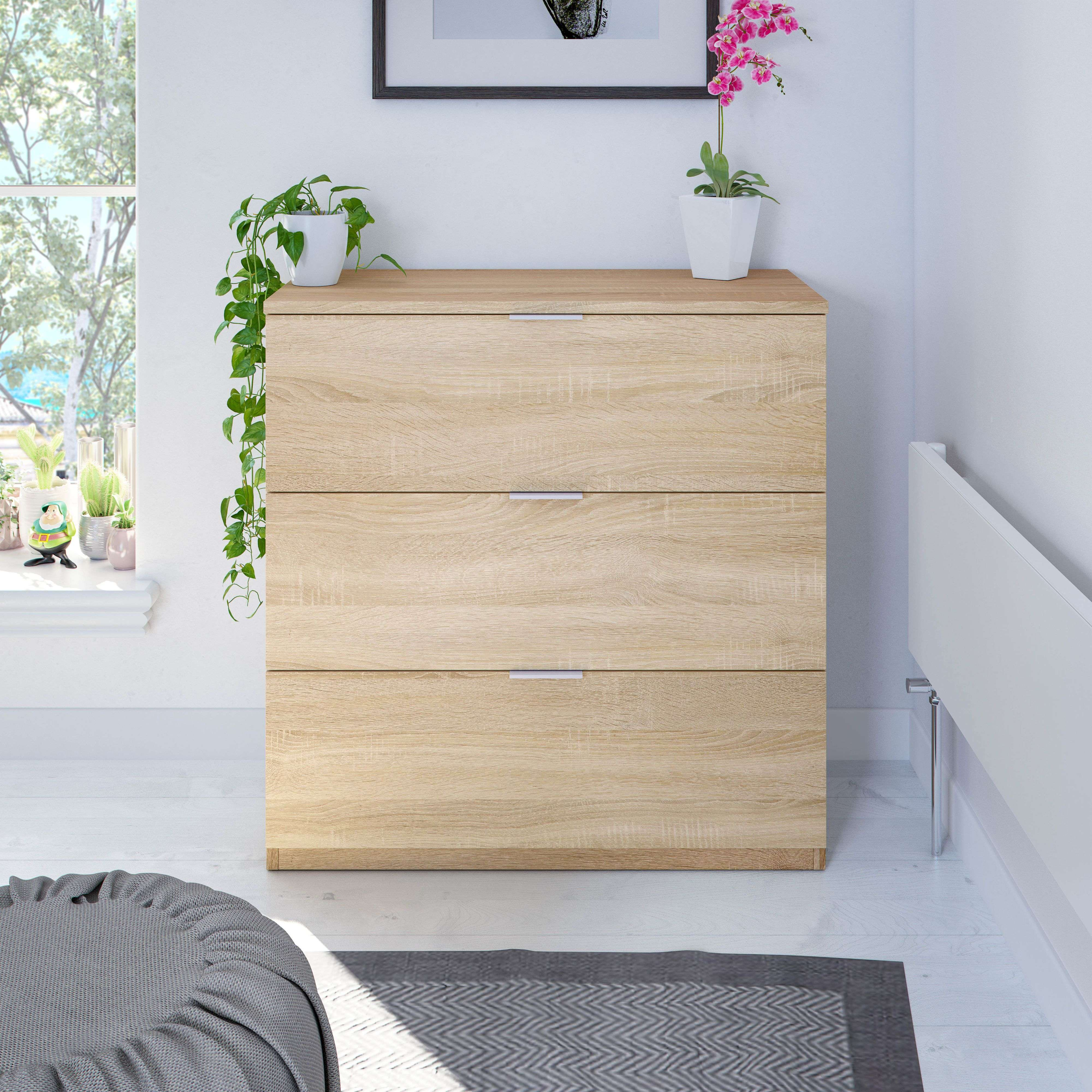 Cómoda de madera con tres cajones, al lado una orquídea y una planta colgante.