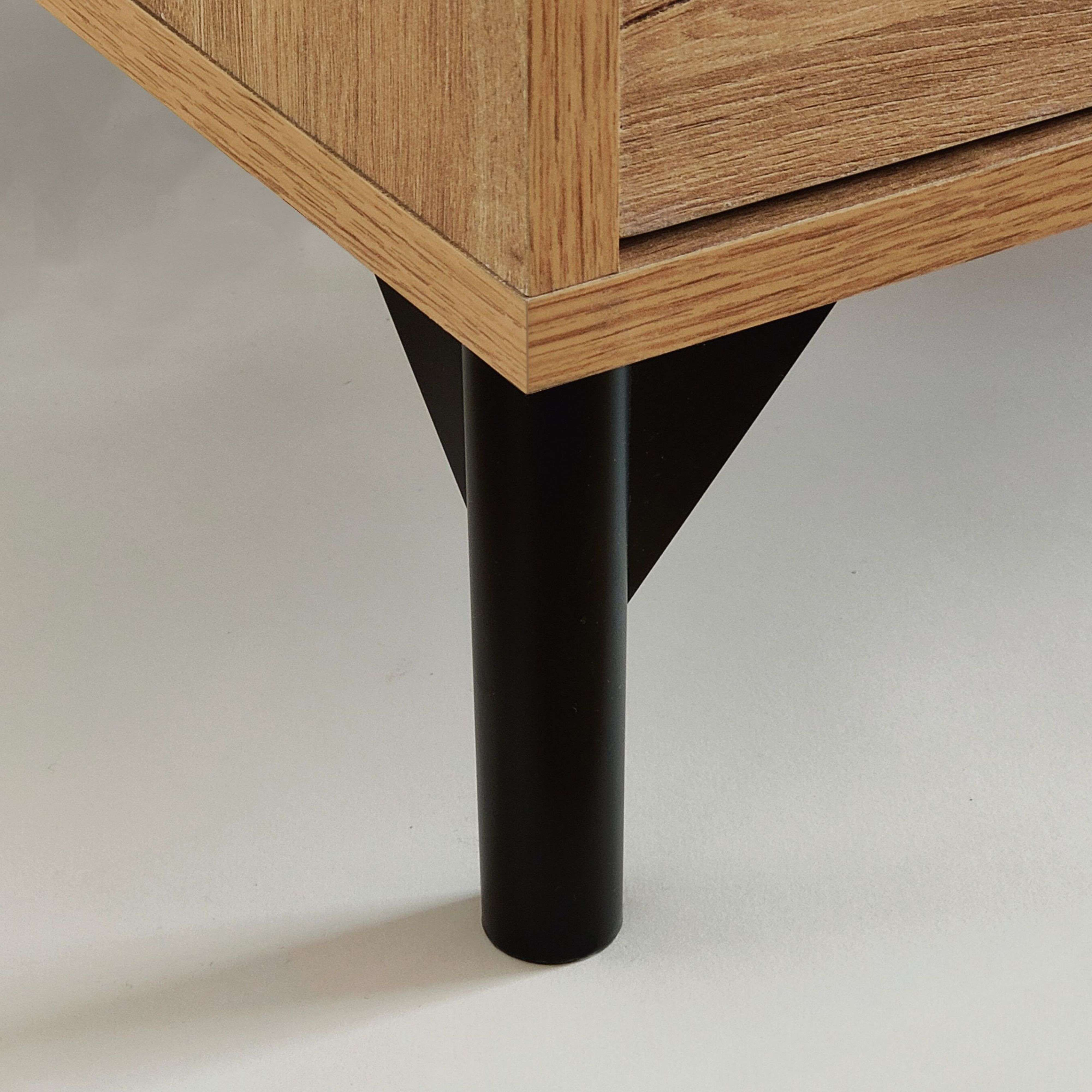Una pata de mueble cilíndrica negra soporta un frente de mueble de madera.