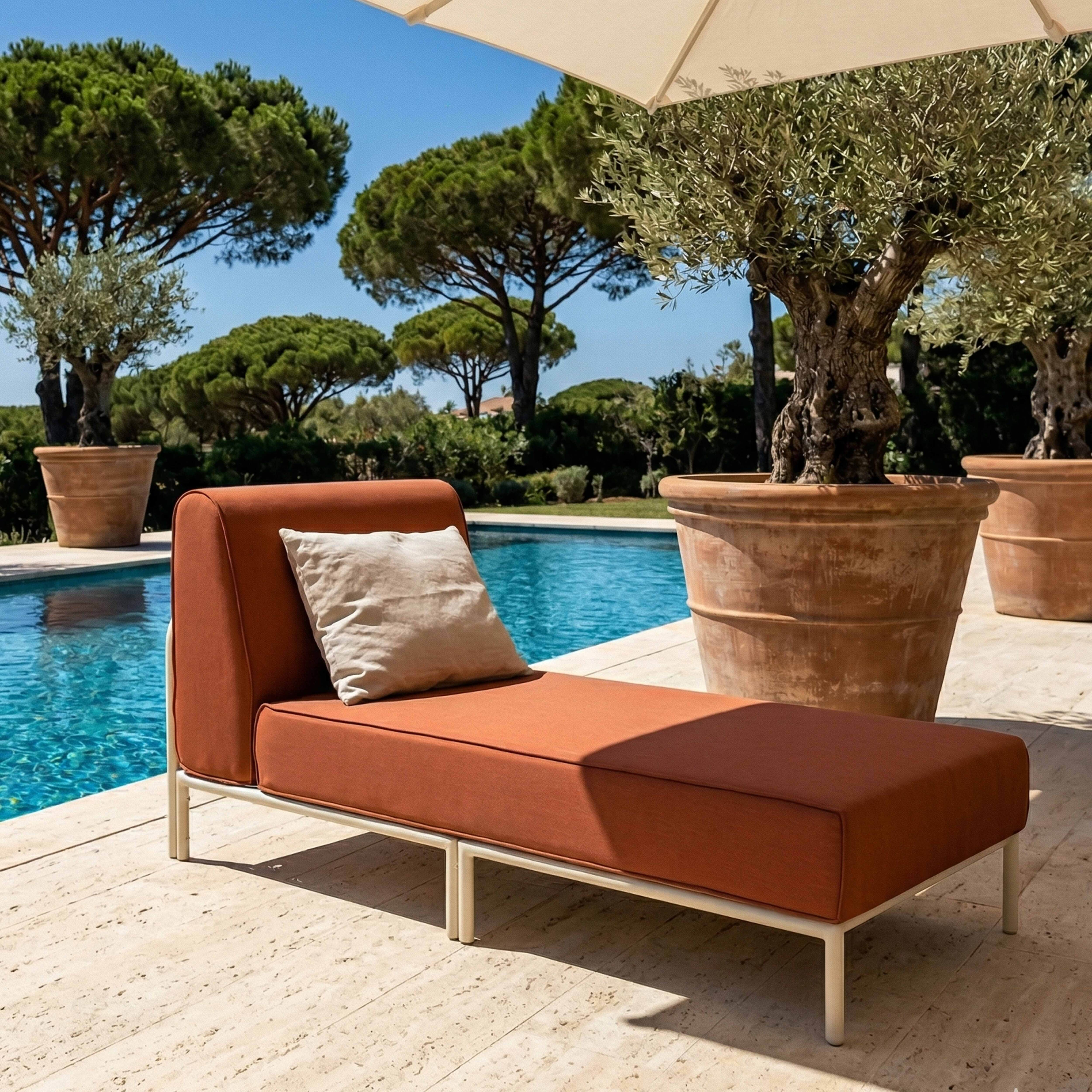 Eine orangefarbene Chaiselongue mit Kissen neben einem Pool mit Bäumen.
