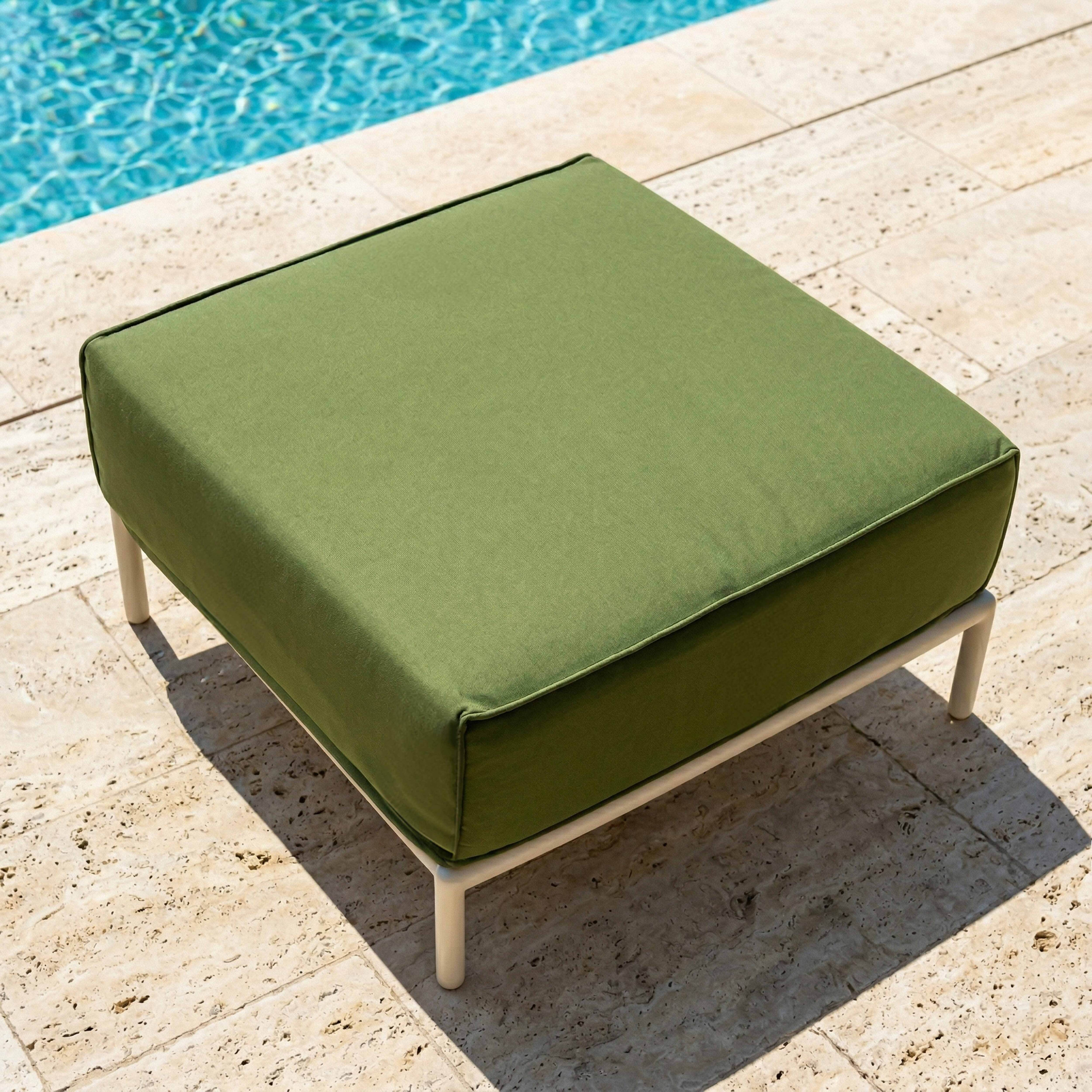 Ein grüner Hocker mit weißen Beinen steht auf einer Steinplatte neben einem Pool.