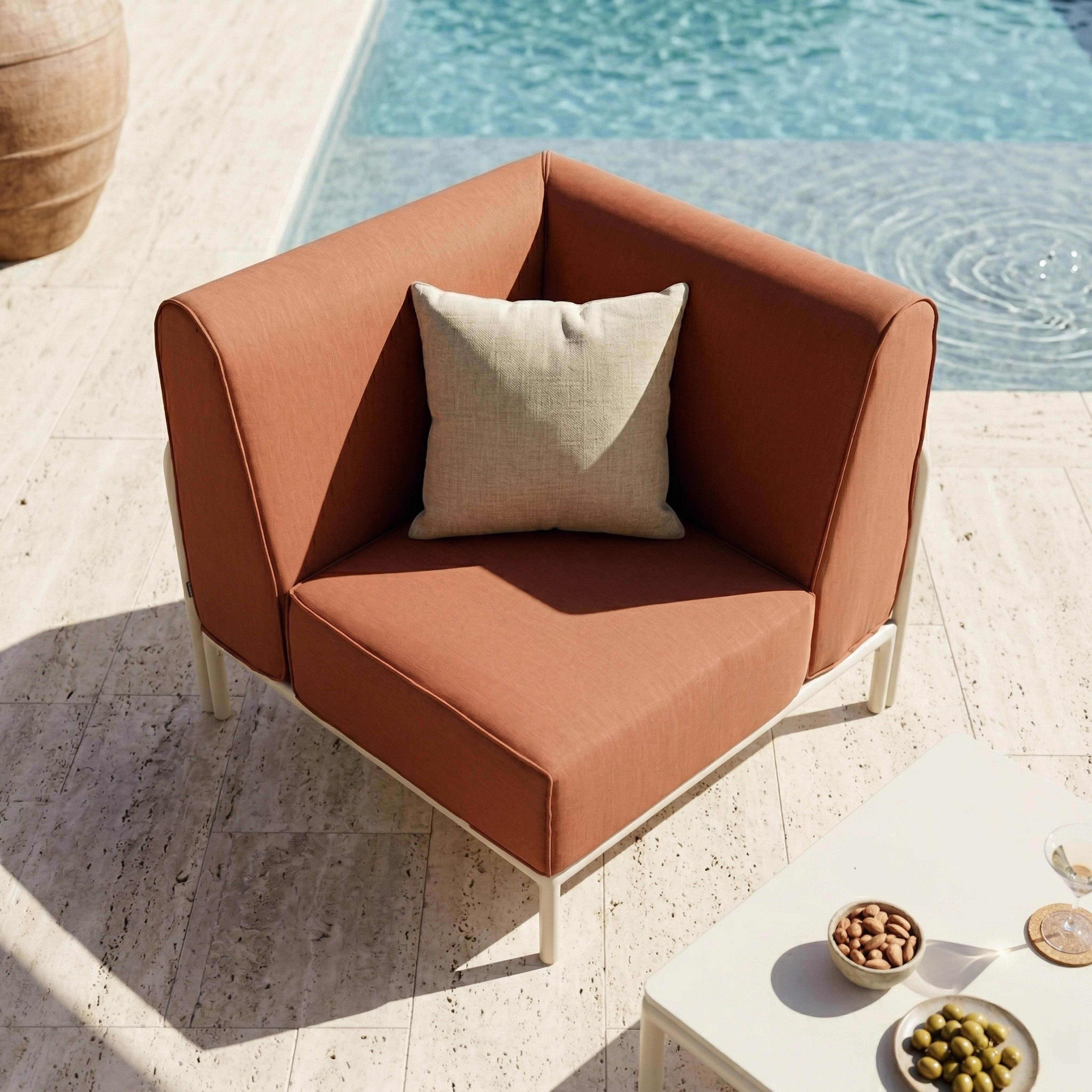 Ein orangefarbener Eckstuhl mit Kissen neben einem Pool auf einer gefliesten Terrasse.