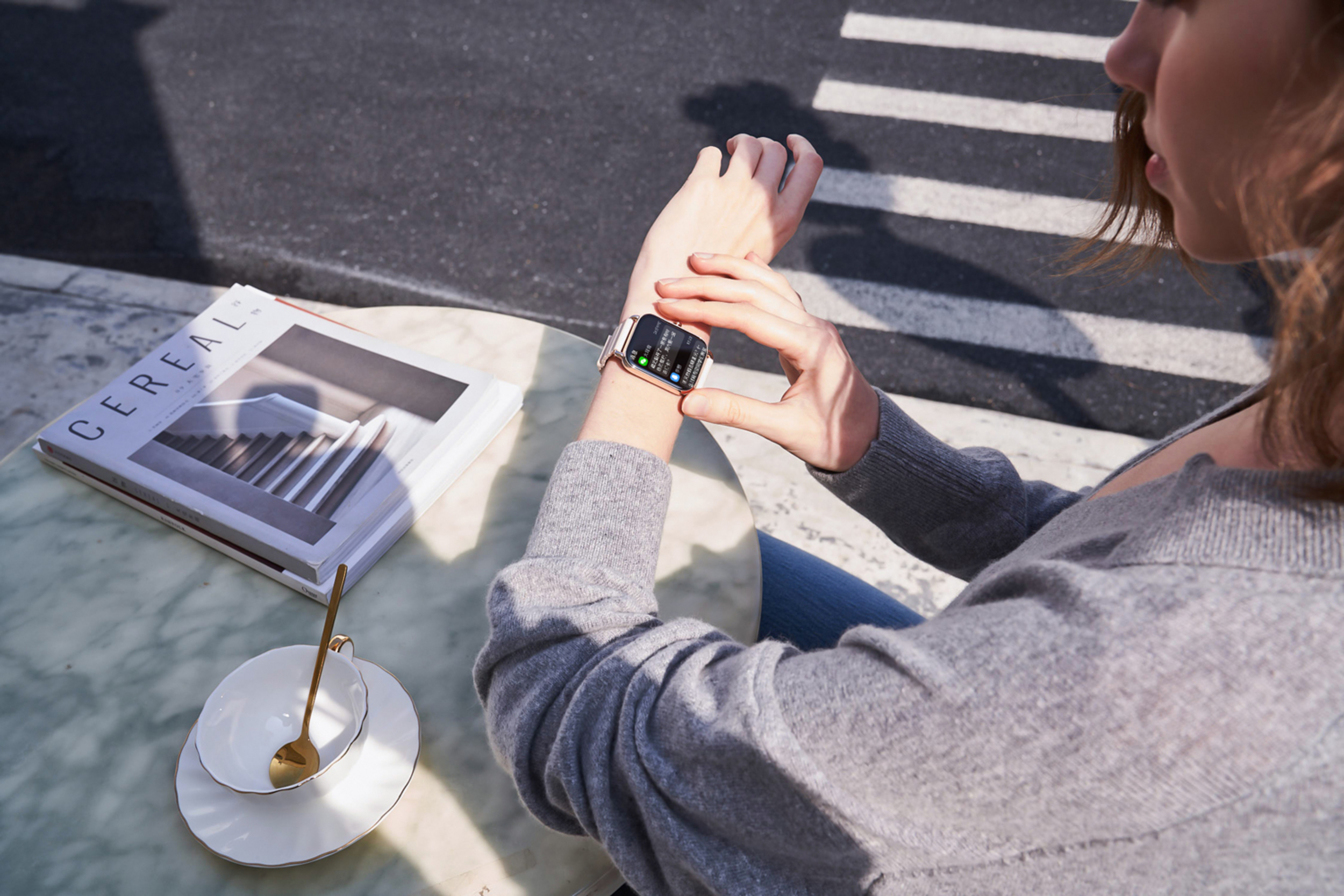 Person schaut auf ihre Smartwatch neben einem Magazin und einer Tasse.