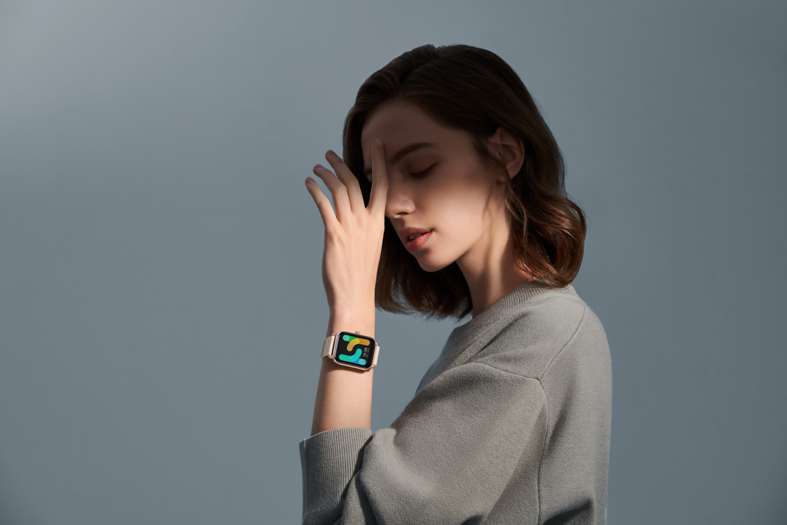 Frau mit der Hand im Gesicht, trägt eine Smartwatch mit buntem Zifferblatt.