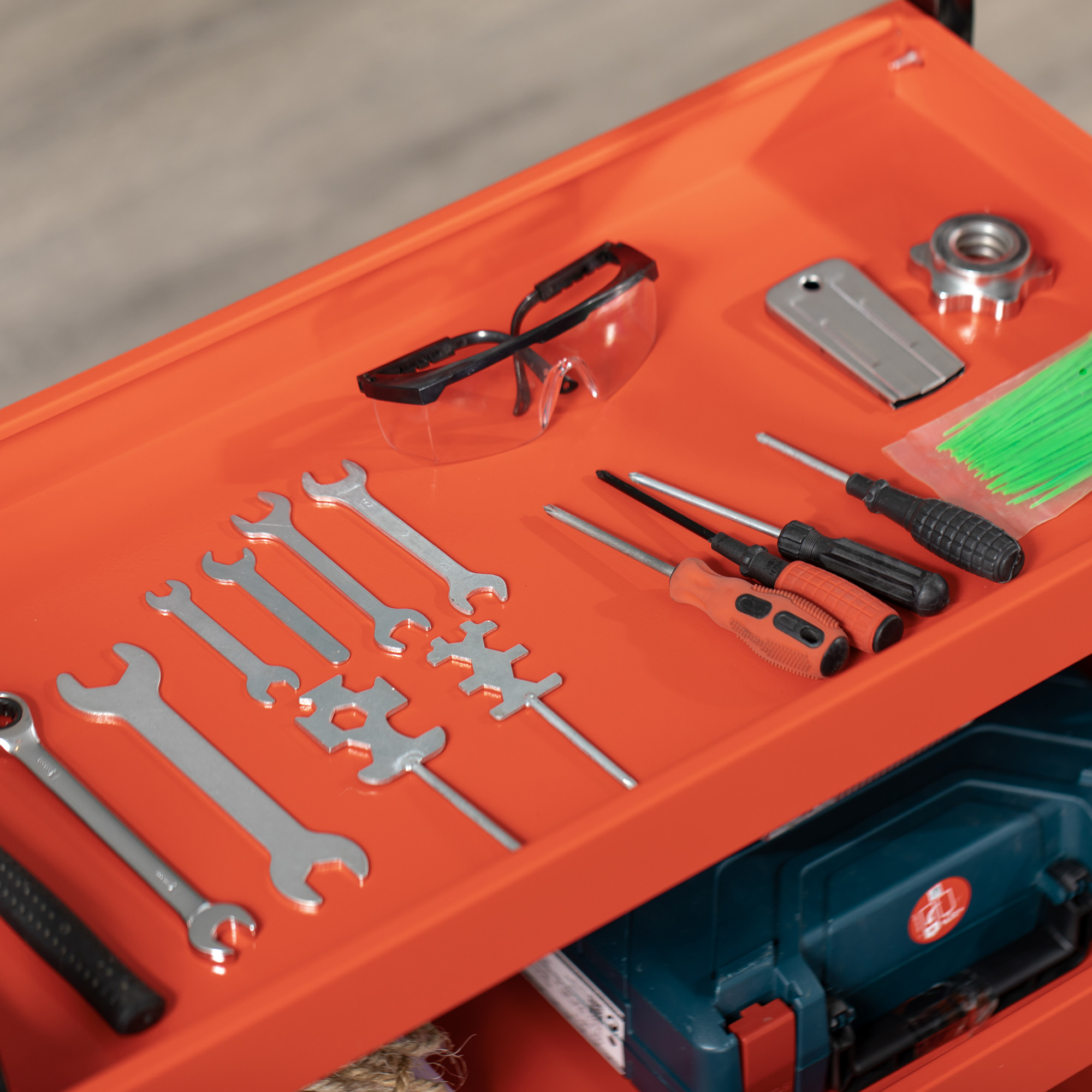 Carro de herramientas naranja con llaves, destornilladores, gafas de seguridad y caja de herramientas azul.