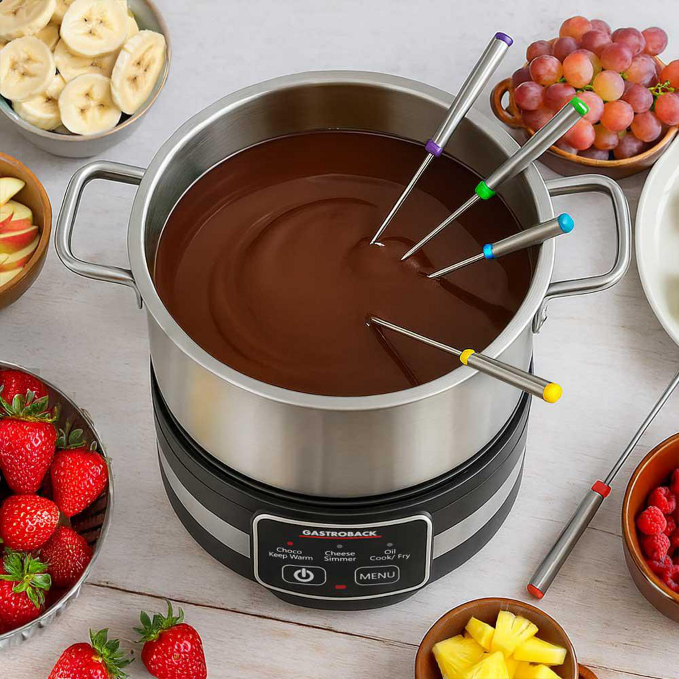 Ein Fonduetopf mit geschmolzener Schokolade, umgeben von Schalen mit Erdbeeren, Bananen, Trauben und Ananas.