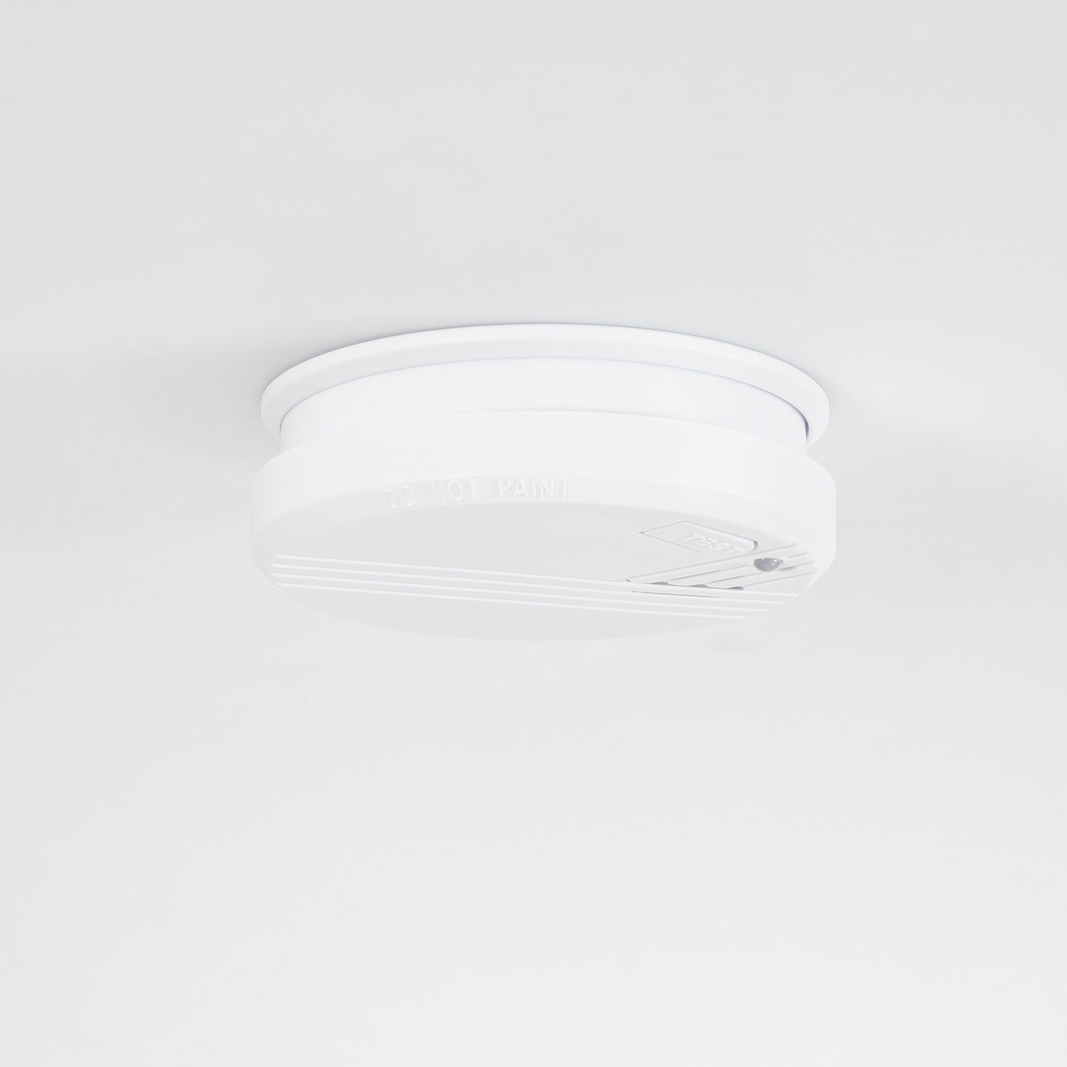 A white smoke detector is mounted on a white ceiling.