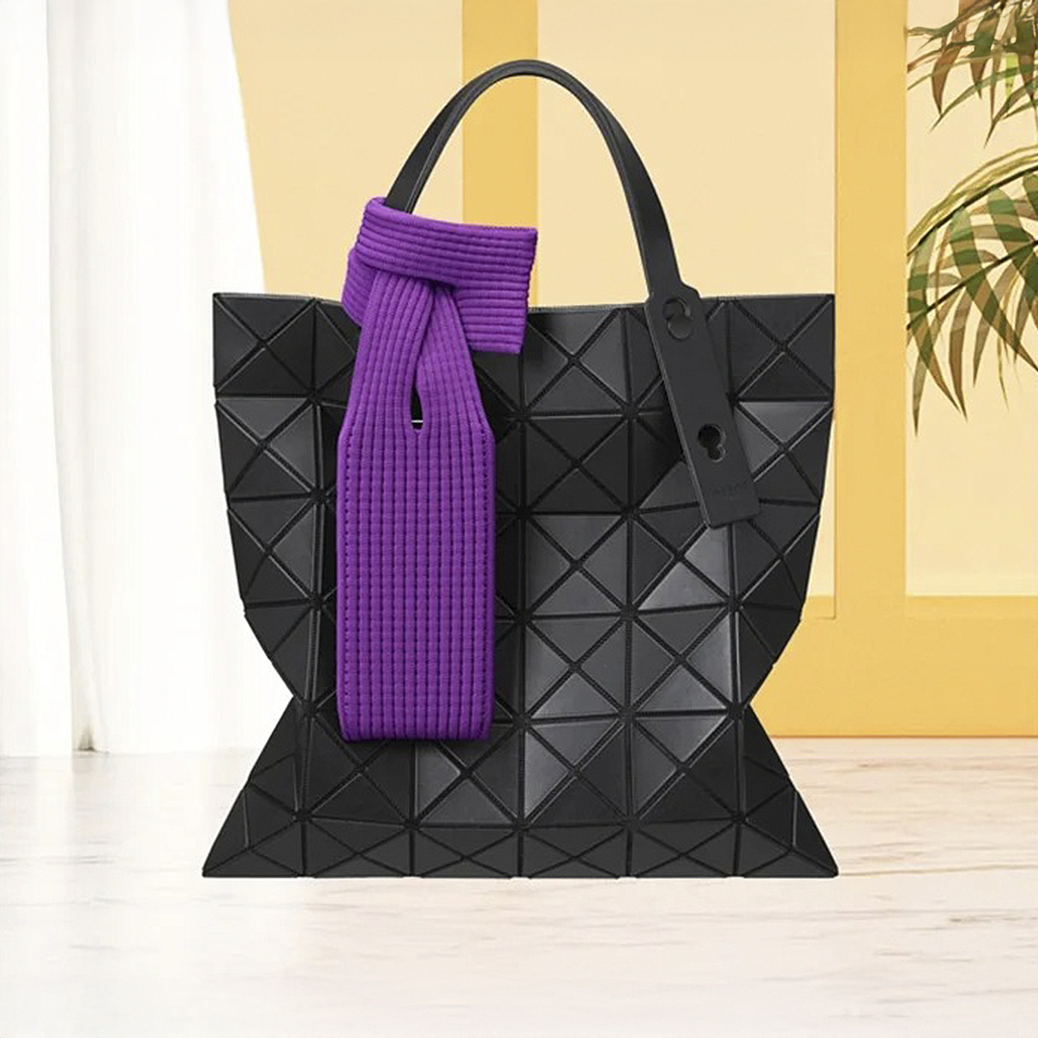 Una borsa geometrica nera con una sciarpa viola legata ai manici.