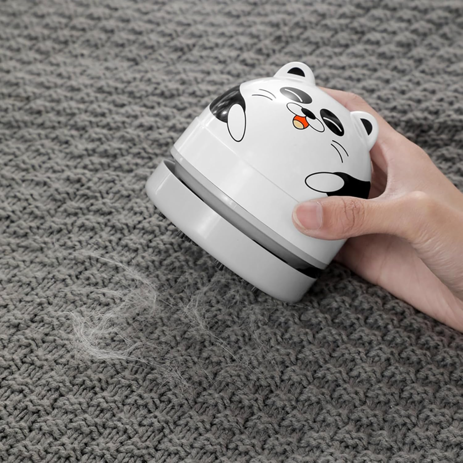 Ein weißer Fusselentferner in Pandaform wird über grauen Stoff geführt.