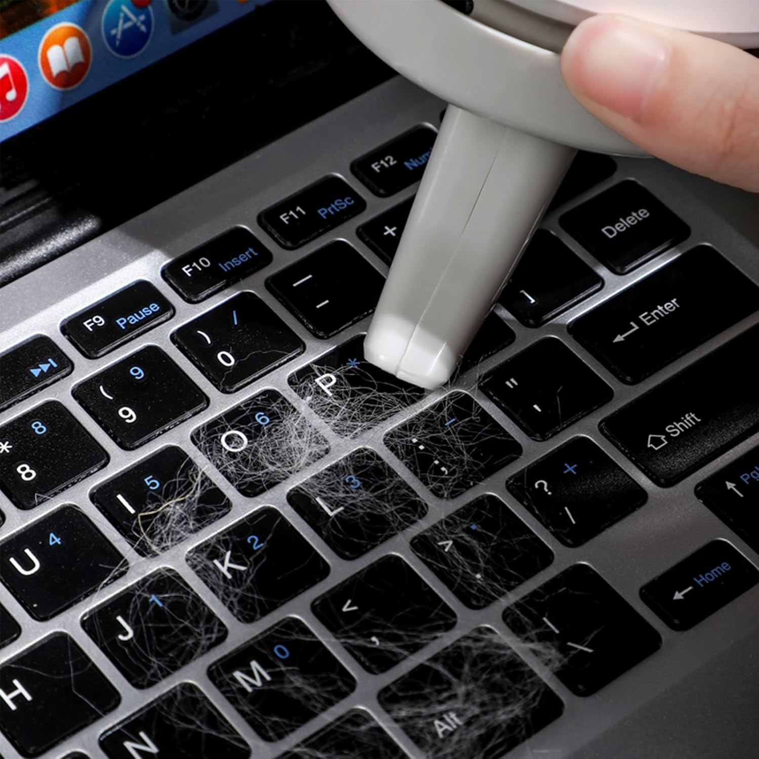 Eine Hand benutzt ein Reinigungswerkzeug auf einer schmutzigen Laptop-Tastatur voller Staub und Haare.