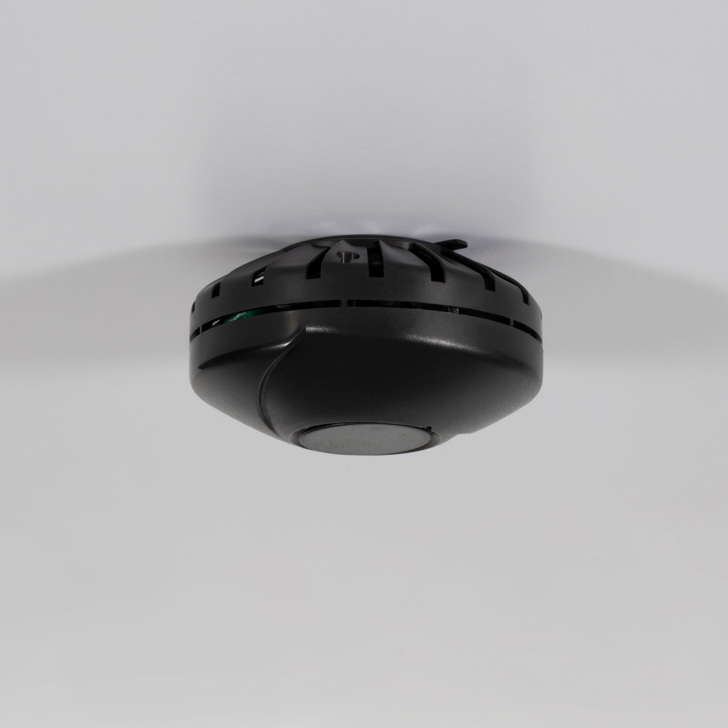 Black smoke detector mounted on a white ceiling.