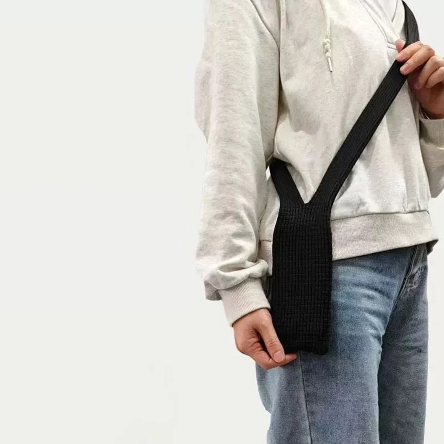 Una persona indossa una felpa grigia, jeans blu e una borsa a tracolla nera.