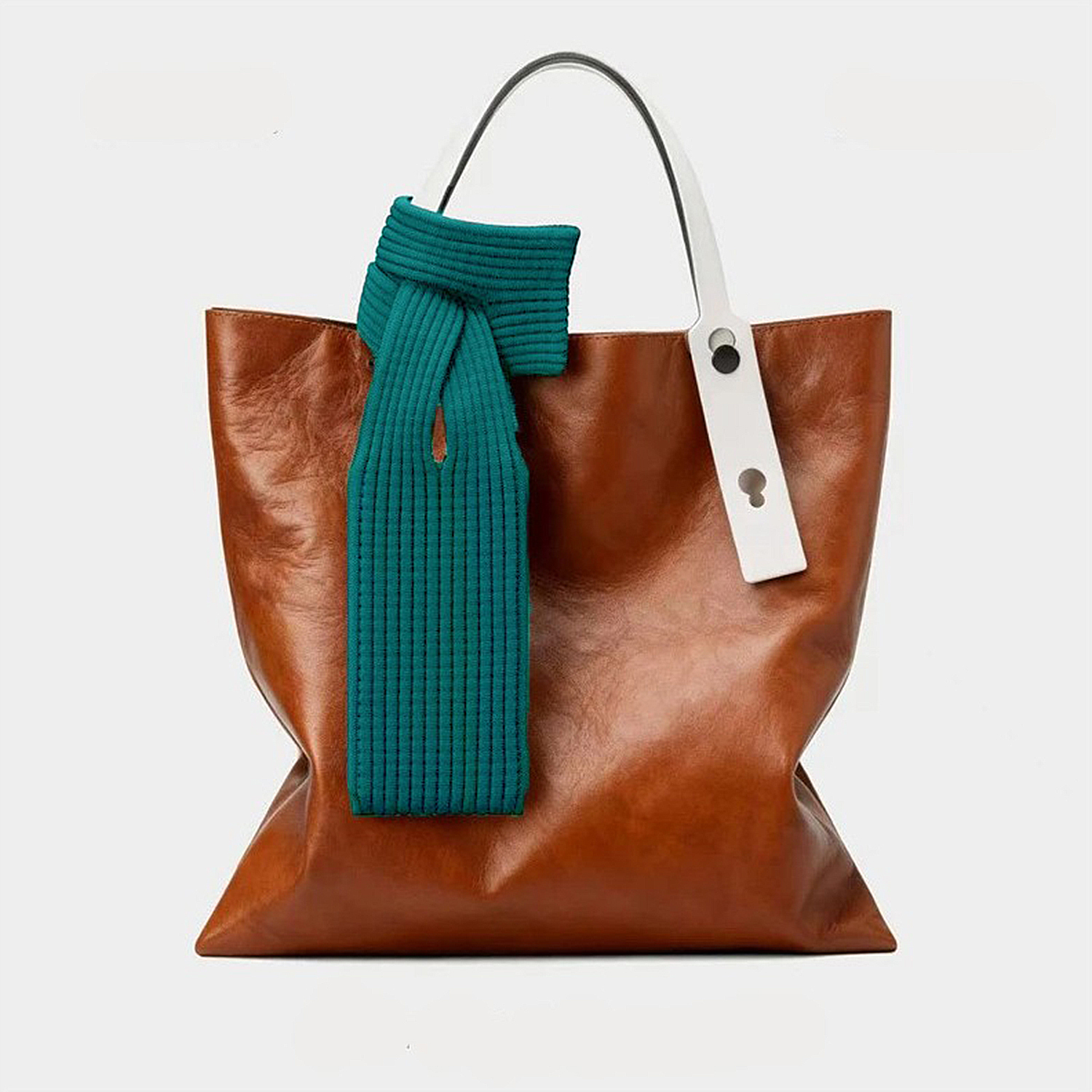 Una borsa tote in pelle marrone con sciarpa verde acqua e manici bianchi.