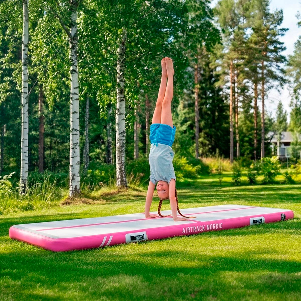 Dziewczynka wykonuje stanie na rękach na dmuchanej macie na zewnątrz.