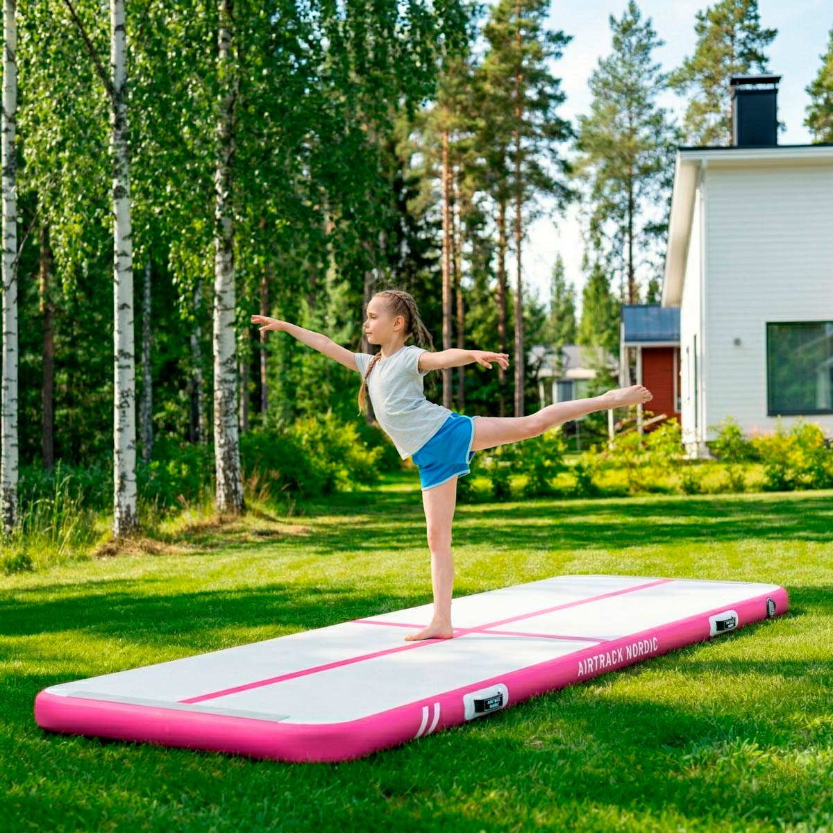 Dziewczynka balansuje na dmuchanej macie w ogrodzie, przyjmując pozę baletową.