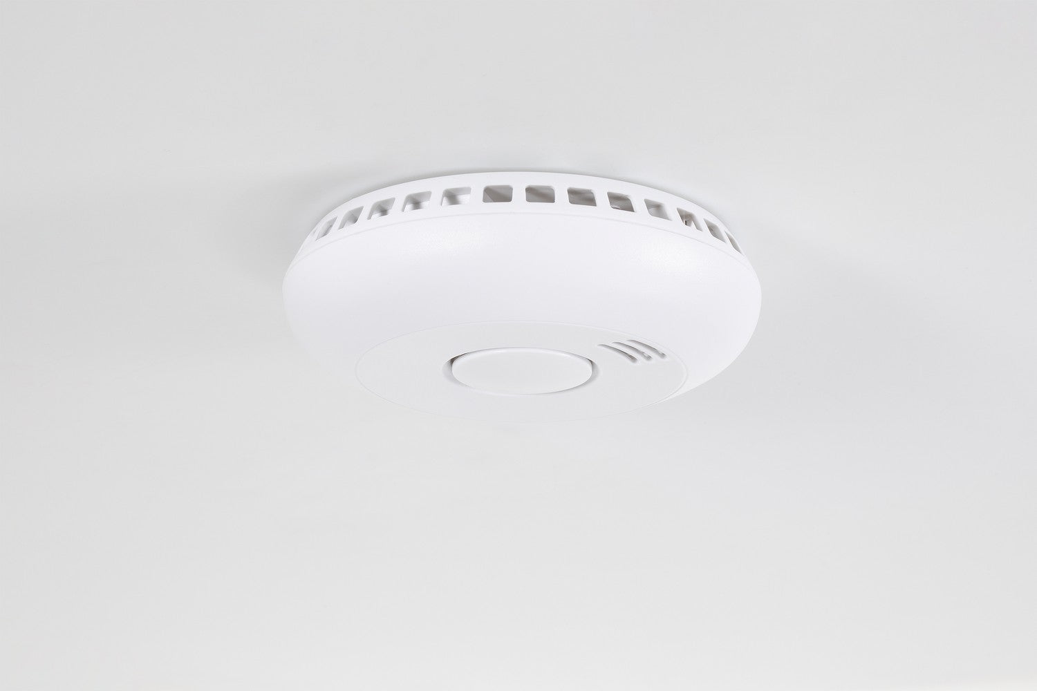 Een witte rookmelder is aan een wit plafond bevestigd.