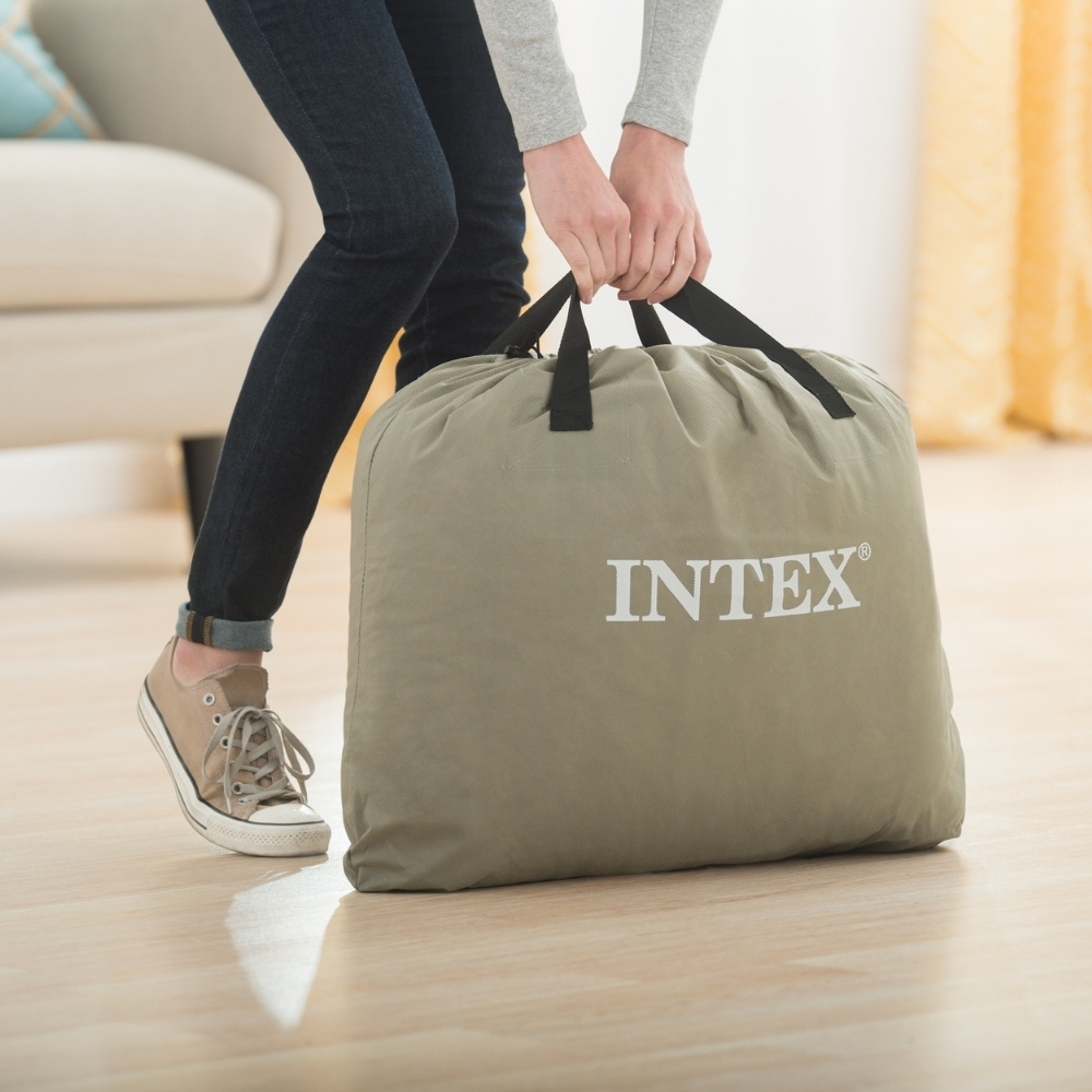 Osoba niosąca oliwkowozieloną torbę z logo INTEX na drewnianej podłodze.