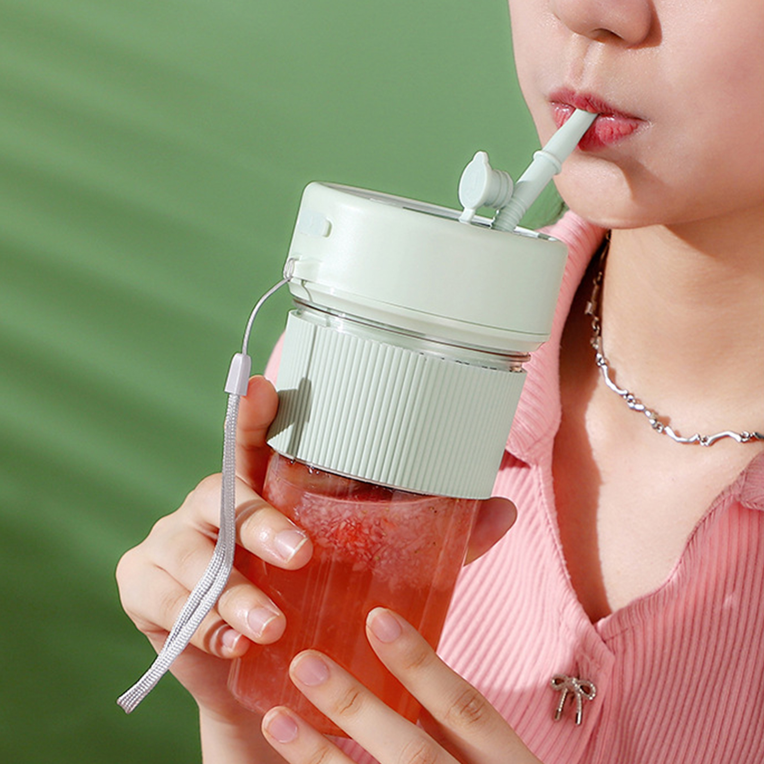 Una persona bebe de un vaso transparente con tapa y pajita verde claro.