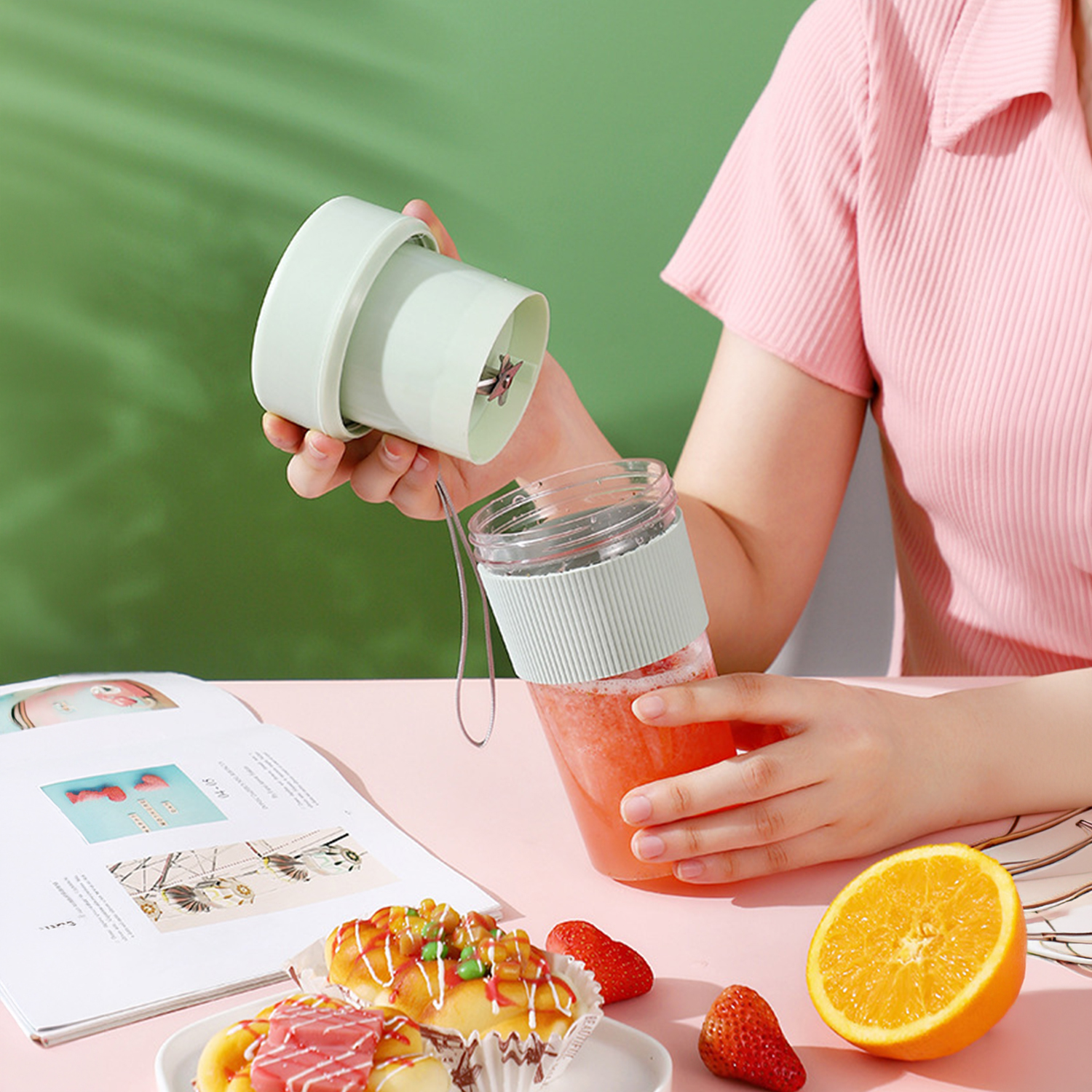 Una persona mezcla jugo rojo en una licuadora portátil sobre una mesa rosa.