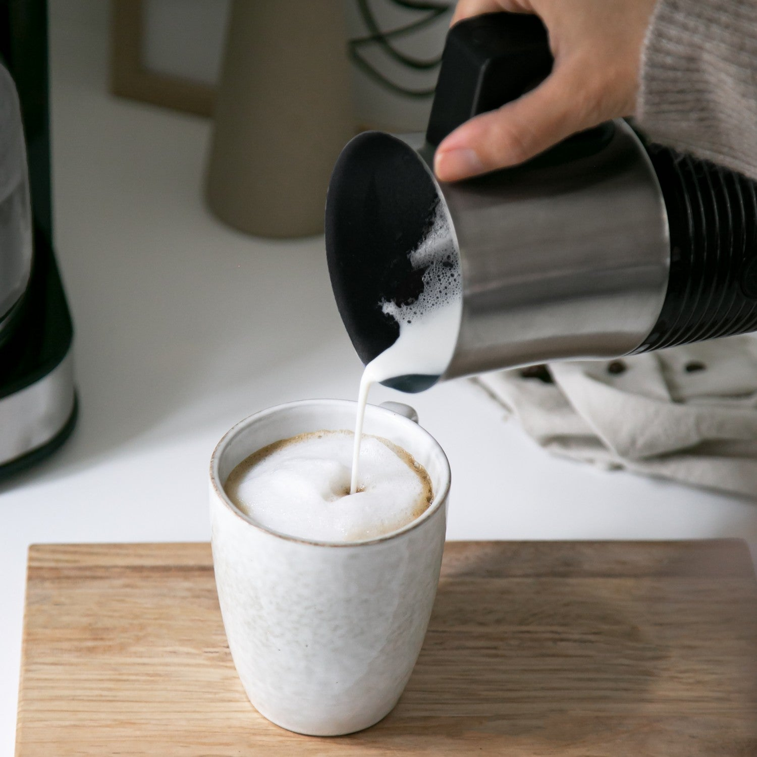 Frothy milk is poured into a coffee cup on a wooden board.