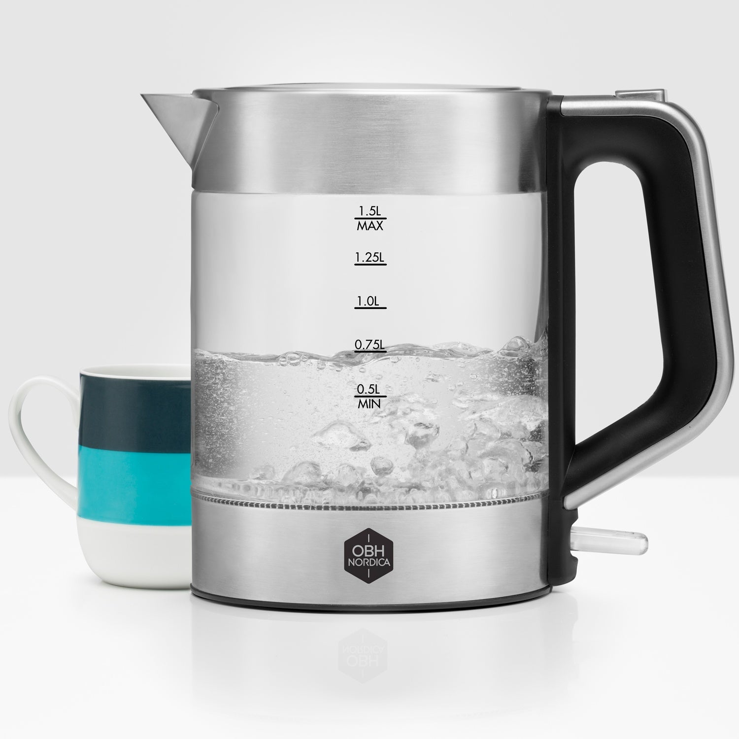 A glass electric kettle with water boiling is next to a striped mug.
