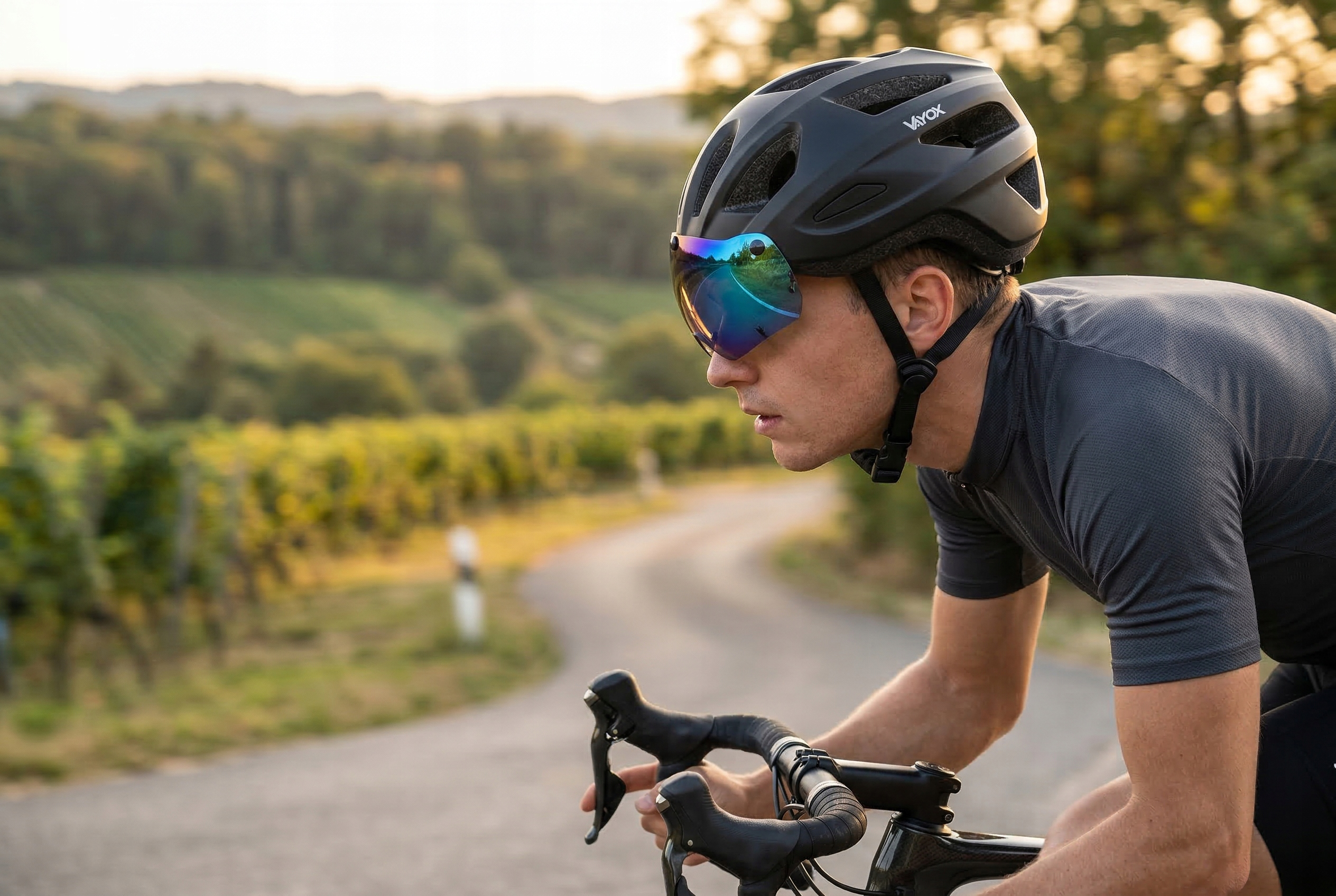 Kolarz w czarnym kasku i szarym stroju kolarskim jedzie po drodze.